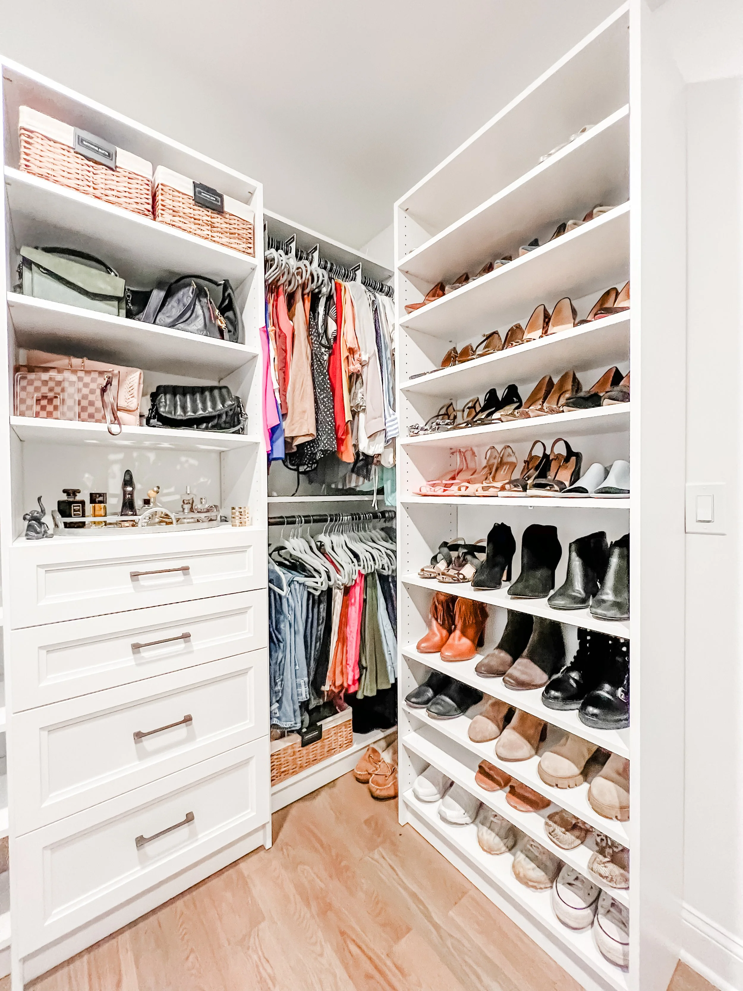 A walk-in closet with white shelving and drawers, containing various shoes, handbags, and clothing.