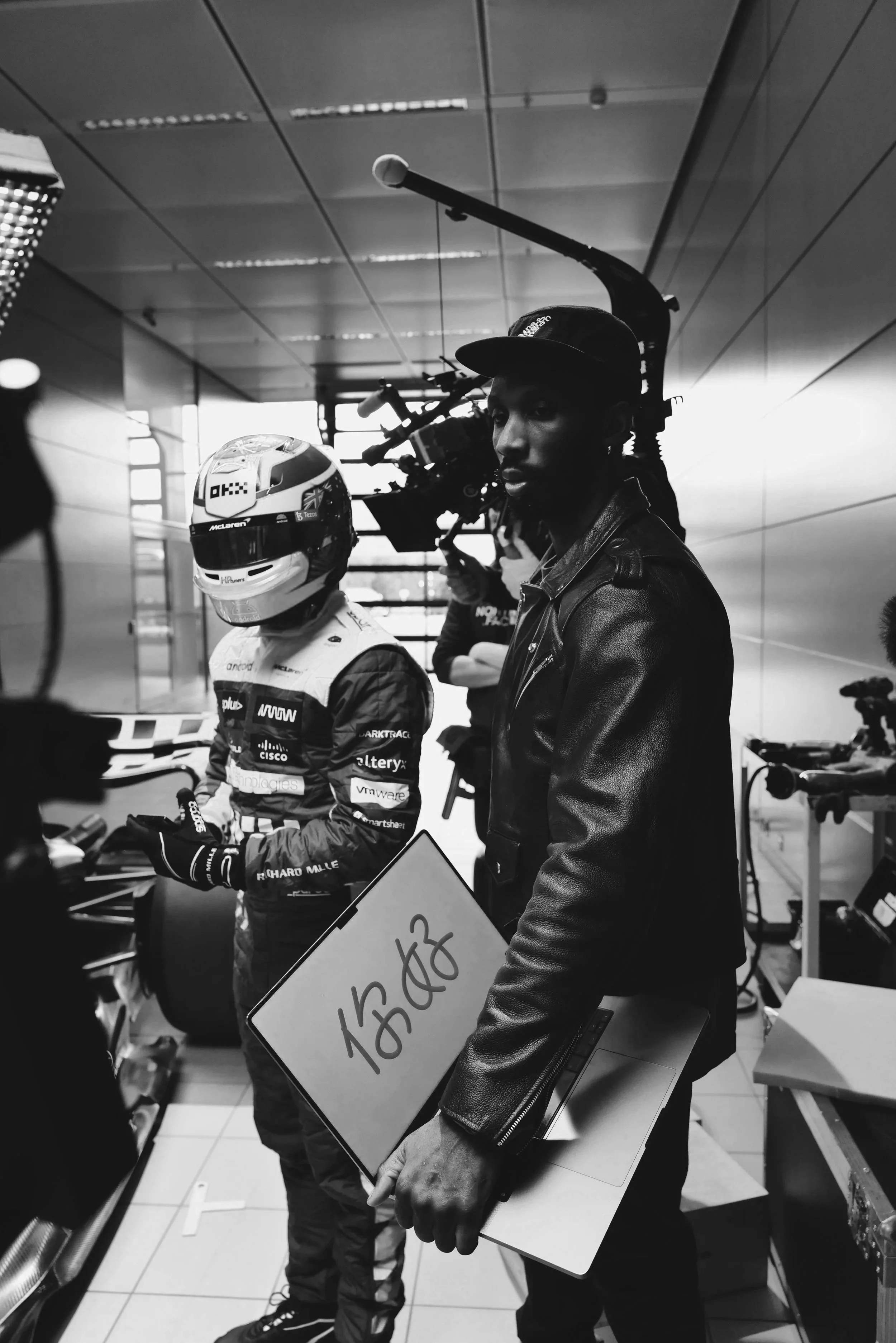 Behind the scenes of ST Davis directing on set at the McLaren Technology Centre in Woking — black and white production still from a Cisco Webex x McLaren F1 commercial shoot in the pit lane garage`
