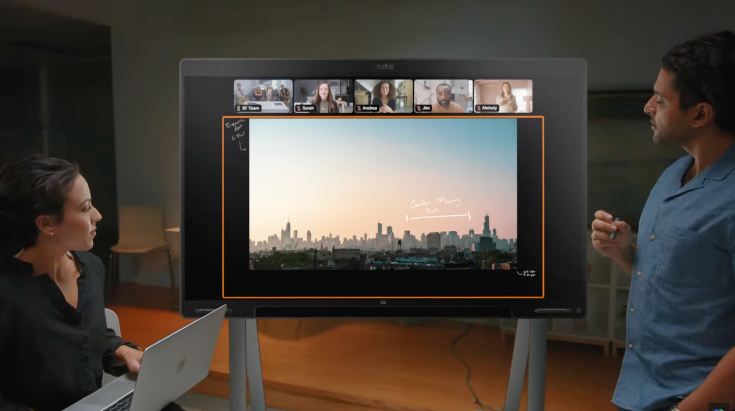 Commercial directed by ST Davis for Apple — two colleagues in a meeting room with a shared presentation on a large display and virtual meeting overhead