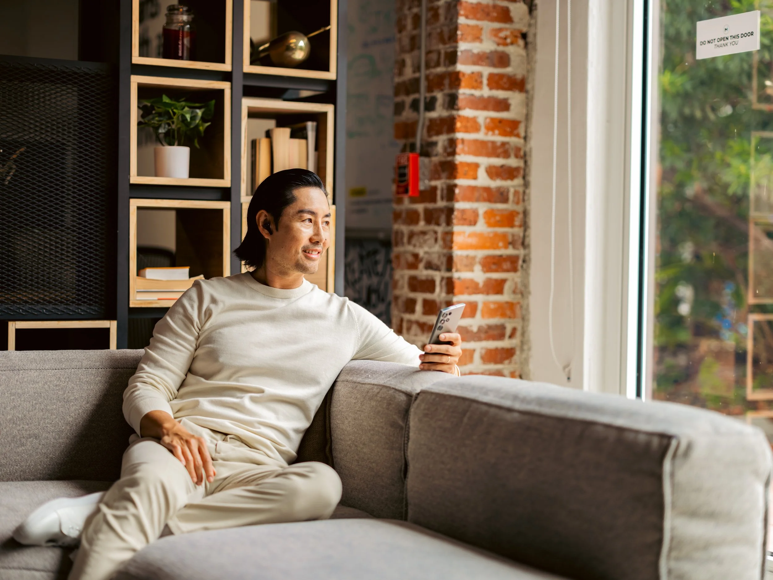 Lifestyle campaign photography by ST Davis for Bang & Olufsen x Cisco — talent relaxing on a sofa with smartphone and wireless earbuds, soft natural window light