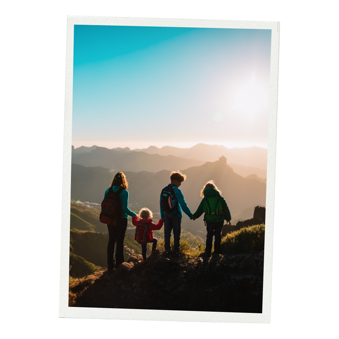 A family of four hiking in the mountains during sunset, holding hands and enjoying the scenic view.