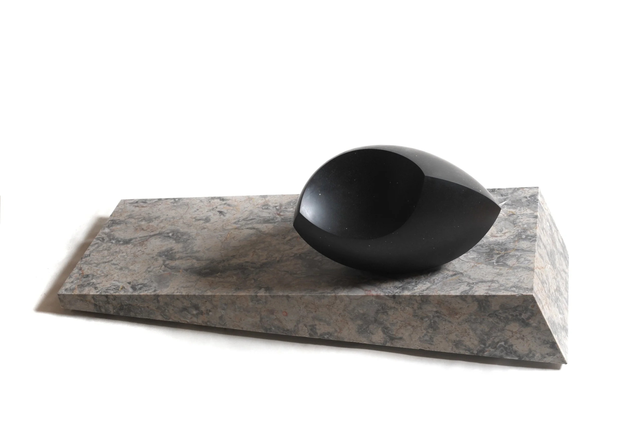 A black, abstract sculpture with a curved shape placed on a rectangular marble slab with gray and beige tones.