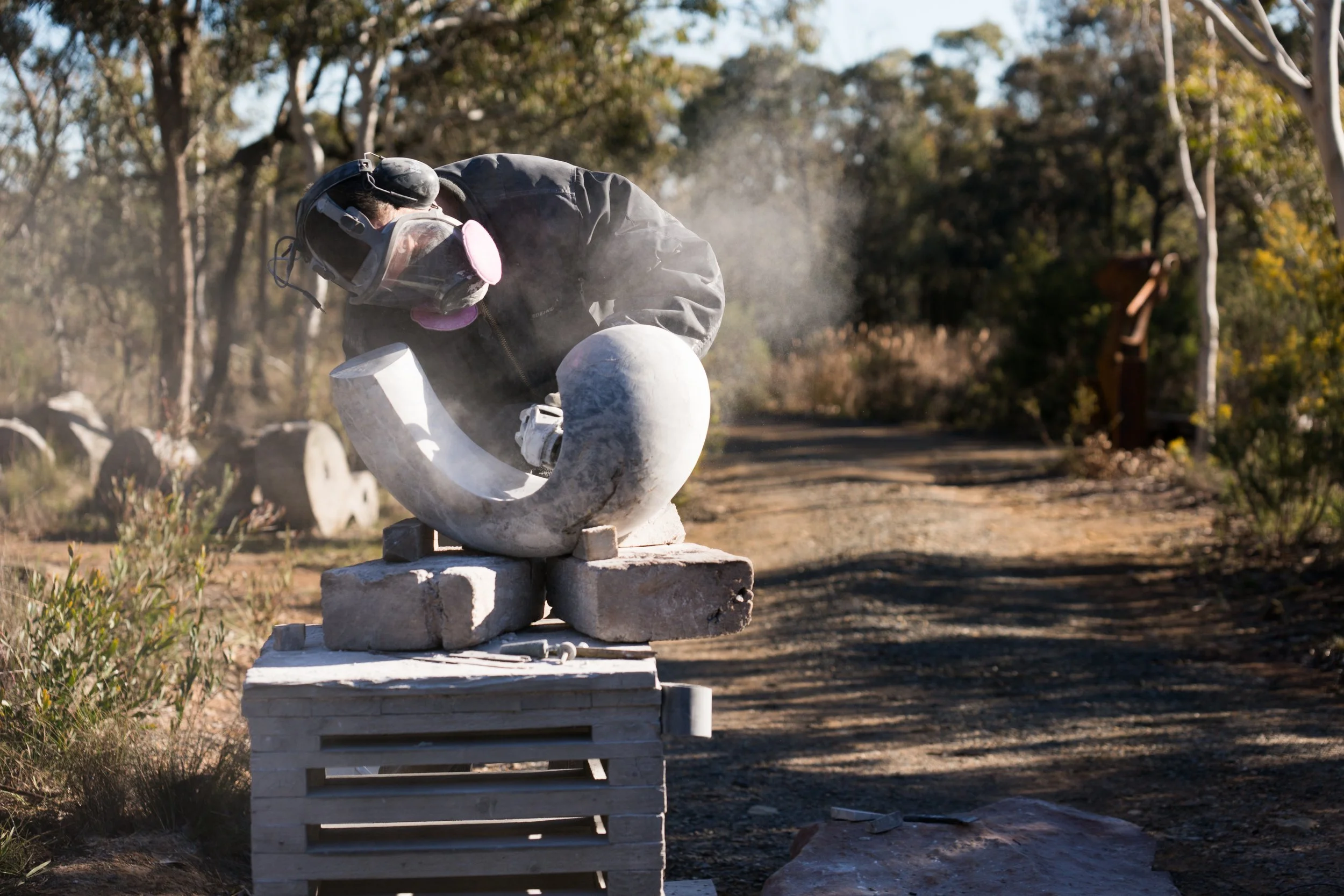 A person wearing protective gear, including a helmet and mask, working outdoors on a stone sculpture or monument.