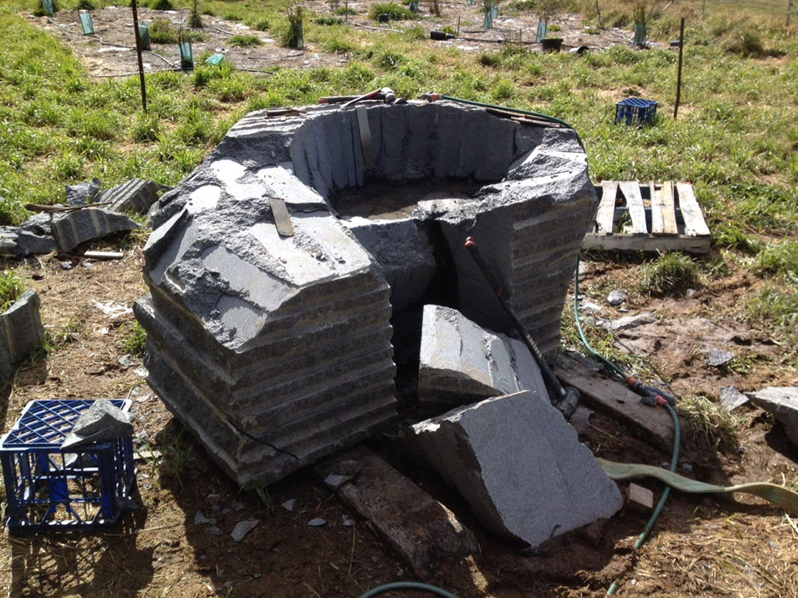 Large stone structure under construction or repair in a grassy outdoor area, with tools and materials scattered around.