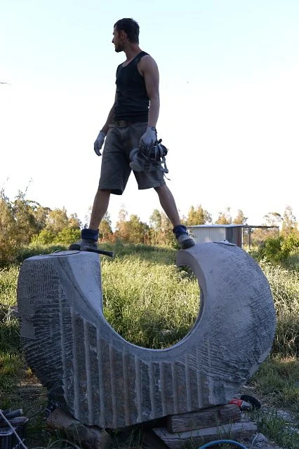 Man standing on a large circular stone sculpture outdoors during daytime.