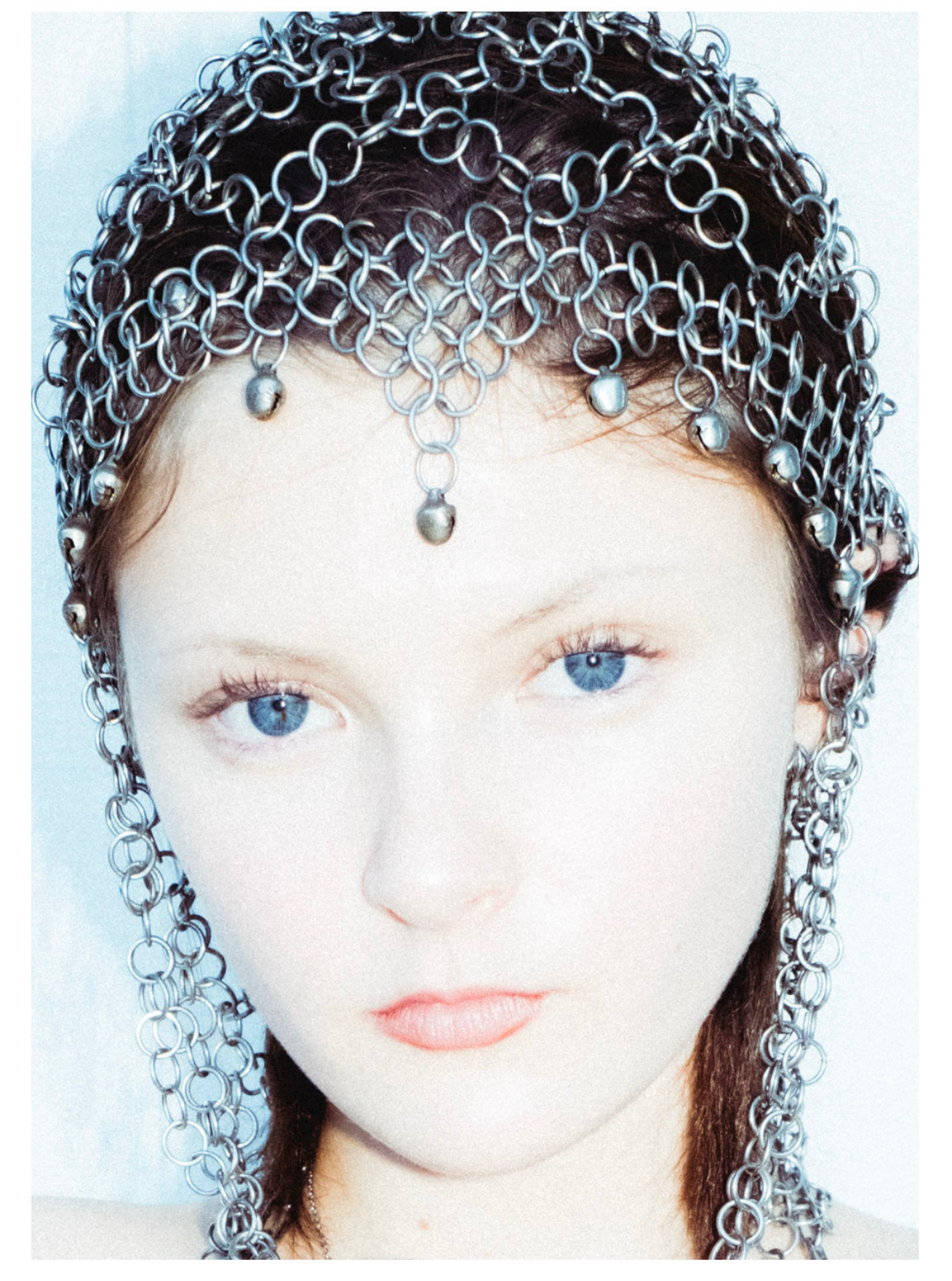 A woman wearing an elaborate headpiece made of interconnected metal rings with small metal spheres hanging from it.