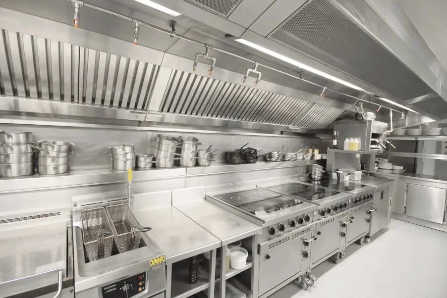 Empty professional commercial kitchen with stainless steel counters, shelves, and appliances.