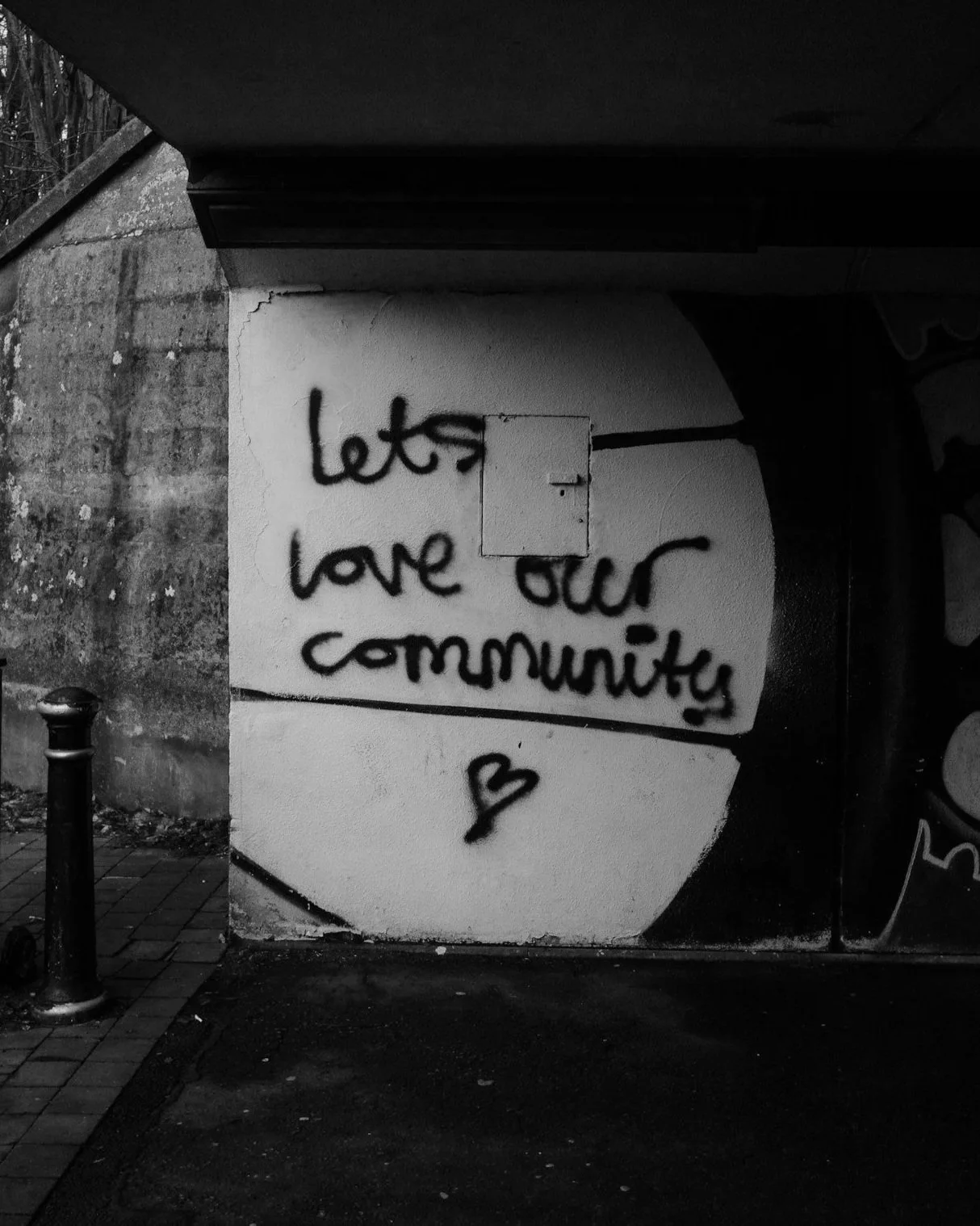 Black and white graffiti on a wall reads "let's love our community" with a small heart underneath.