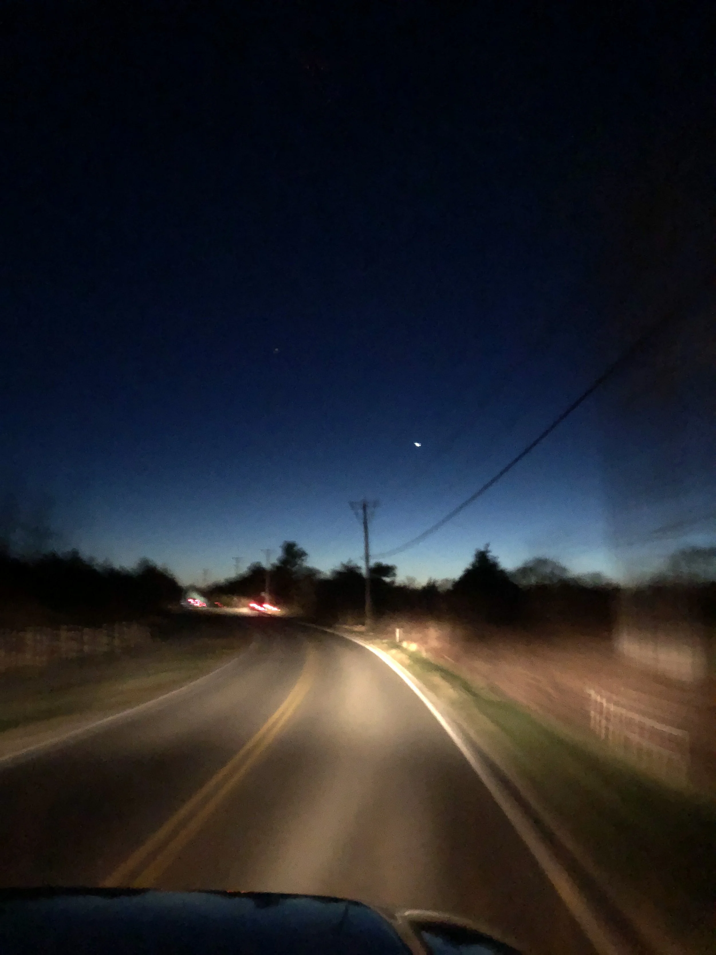 Scenic landscape with a calm lake, rolling grassy hills in the foreground, and tall mountains with rugged peaks in the background under overcast skies.