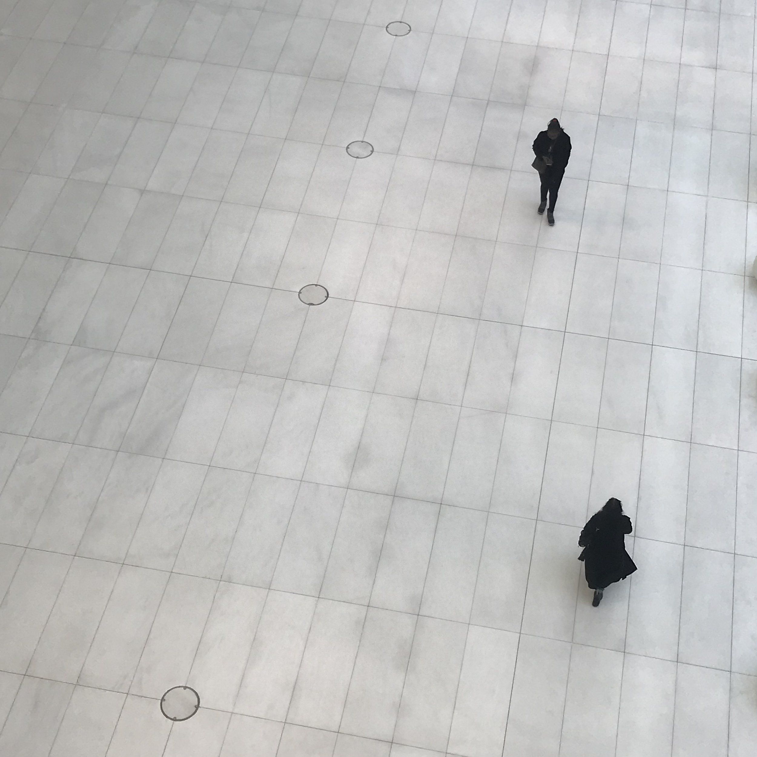 Two people walking across a large white tiled floor viewed from above