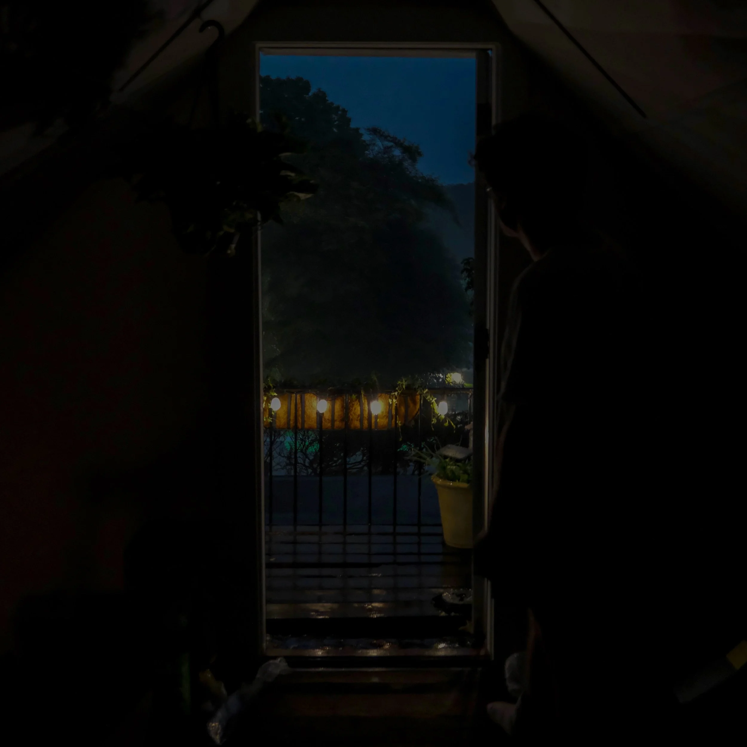 Nighttime view through an open window showing trees and mountains in the distance, with decorative string lights hanging at the bottom of the window.