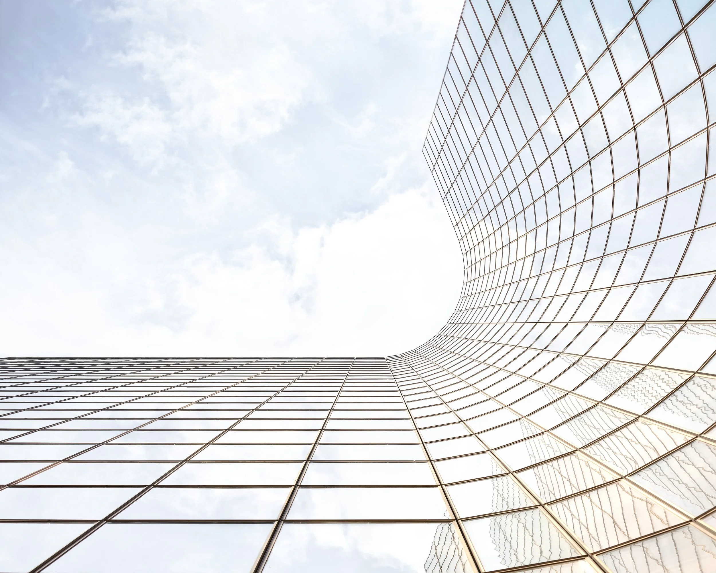 Looking up at a modern glass skyscraper with a curved design against a cloudy sky.