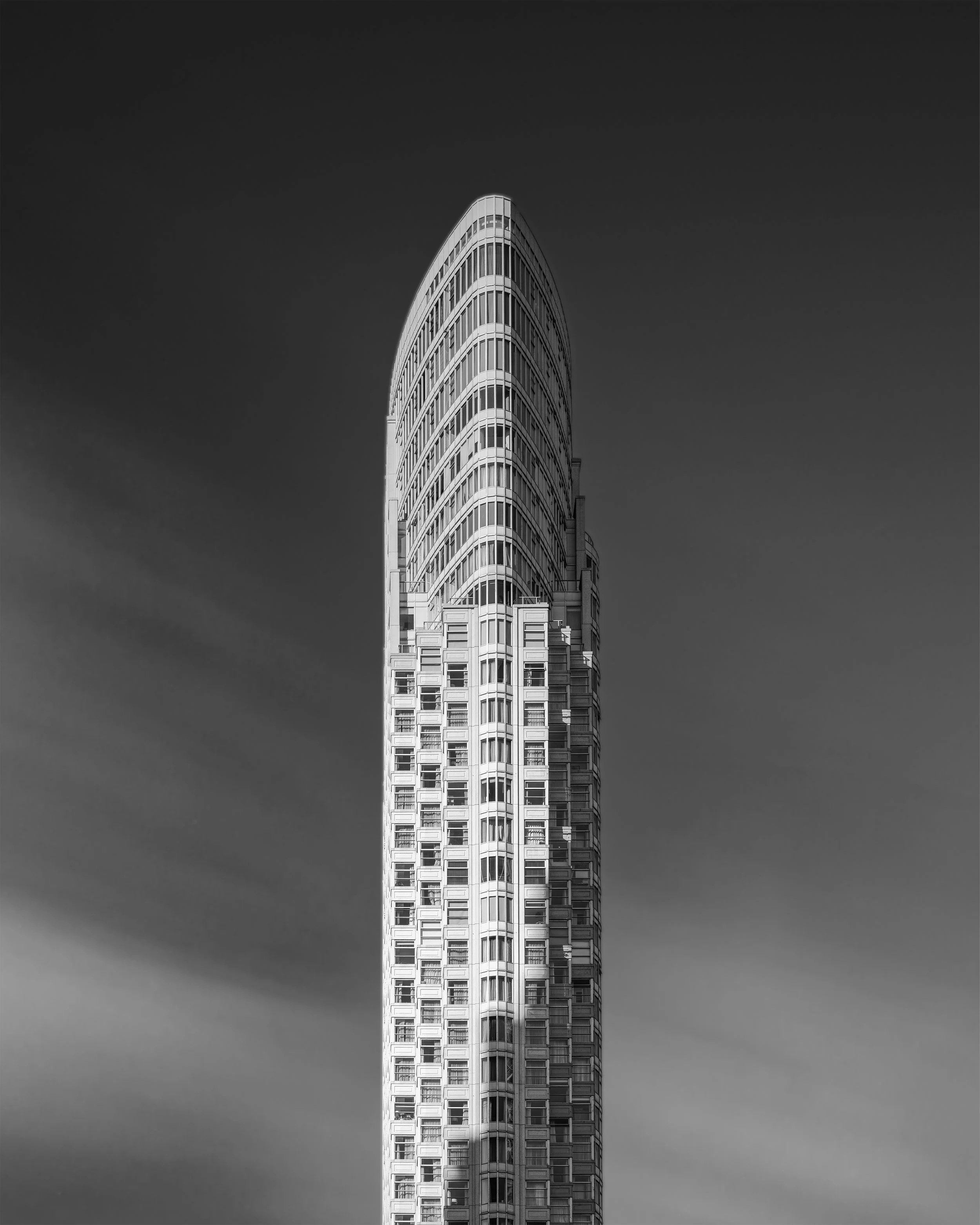 Black and white photo of a tall modern skyscraper with rounded top, clear sky background.