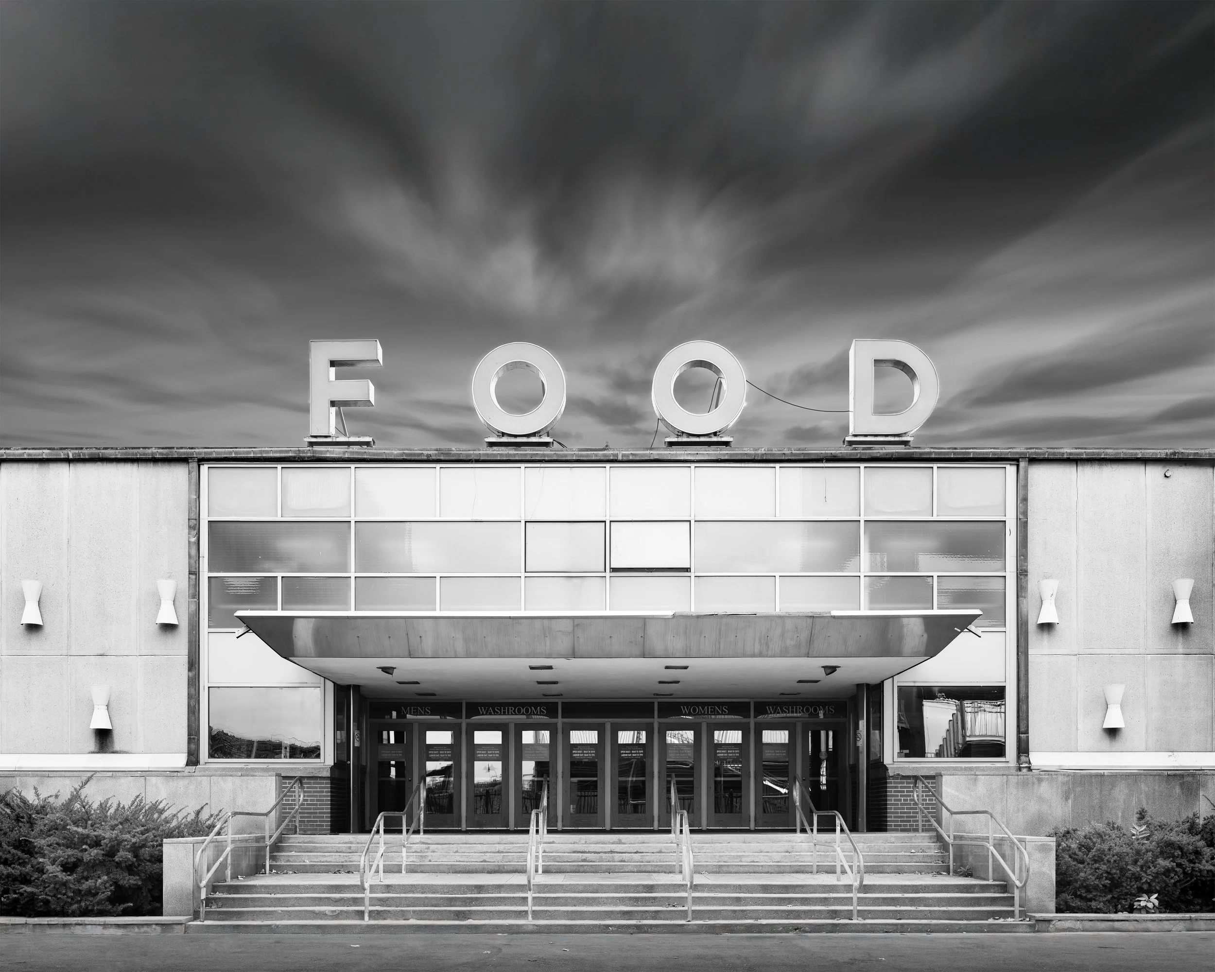 A black and white photo of a building with large letter signs on the roof spelling 'FOOD' against a cloudy sky.