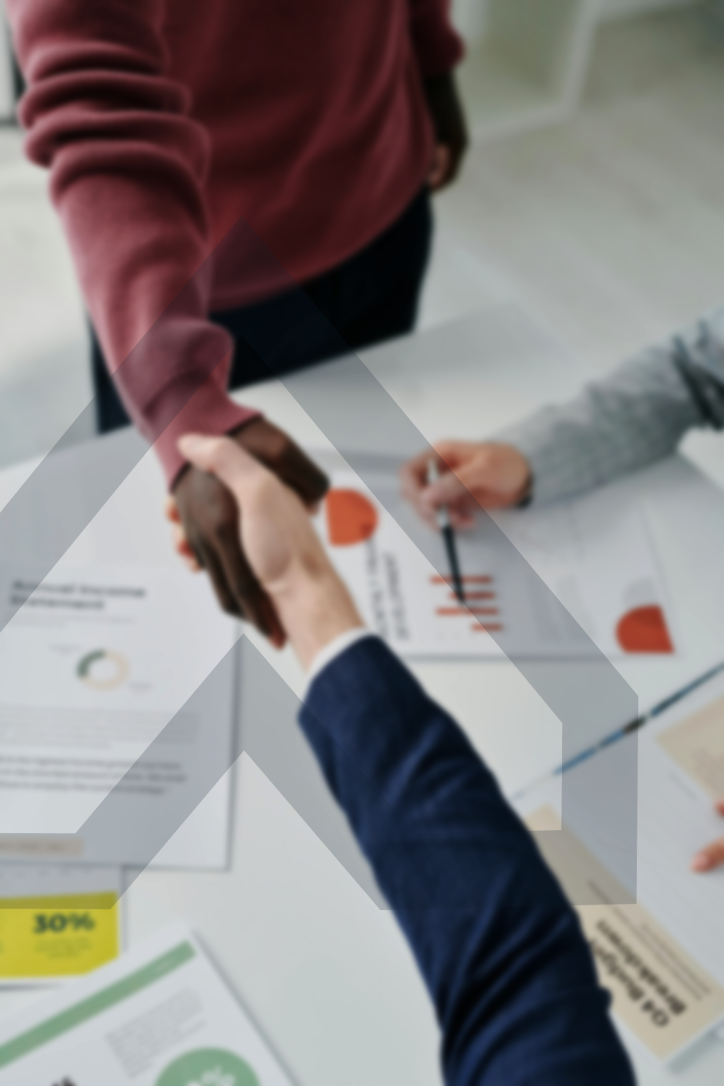 People shaking hands over a table with documents and charts, indicating a business meeting or agreement.