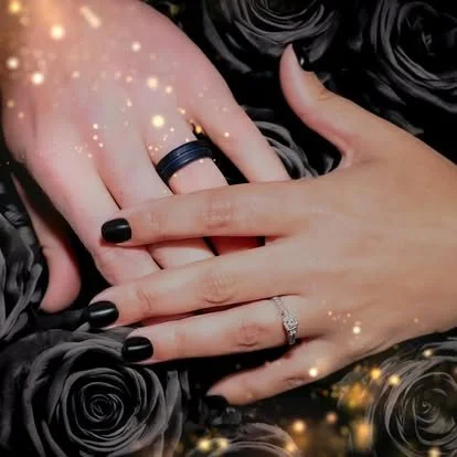 Close-up of two hands with wedding rings, surrounded by black roses and sparkling effects.