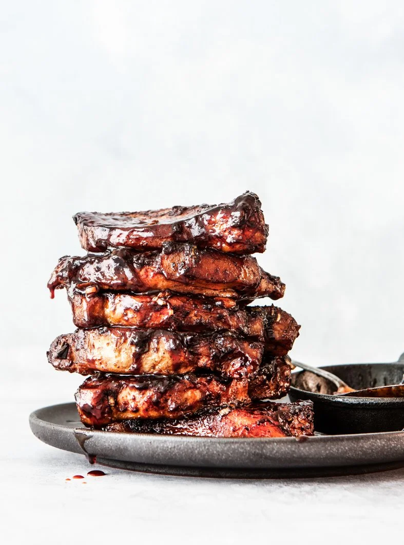 Stack of grilled BBQ pork ribs with a dark glaze on a black plate