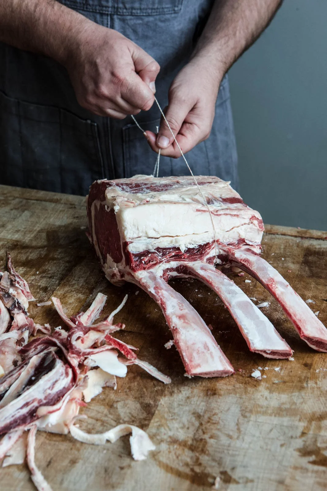 Person butchering a large cut of beef on a wooden cutting board.