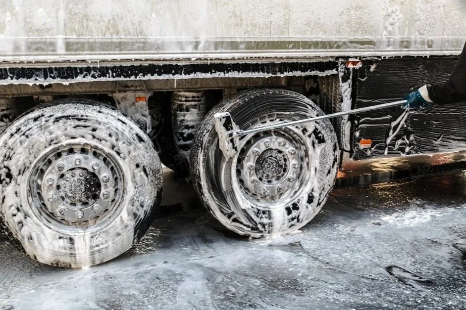 Person cleaning truck tires with a pressure washer, soap and foam on tires.