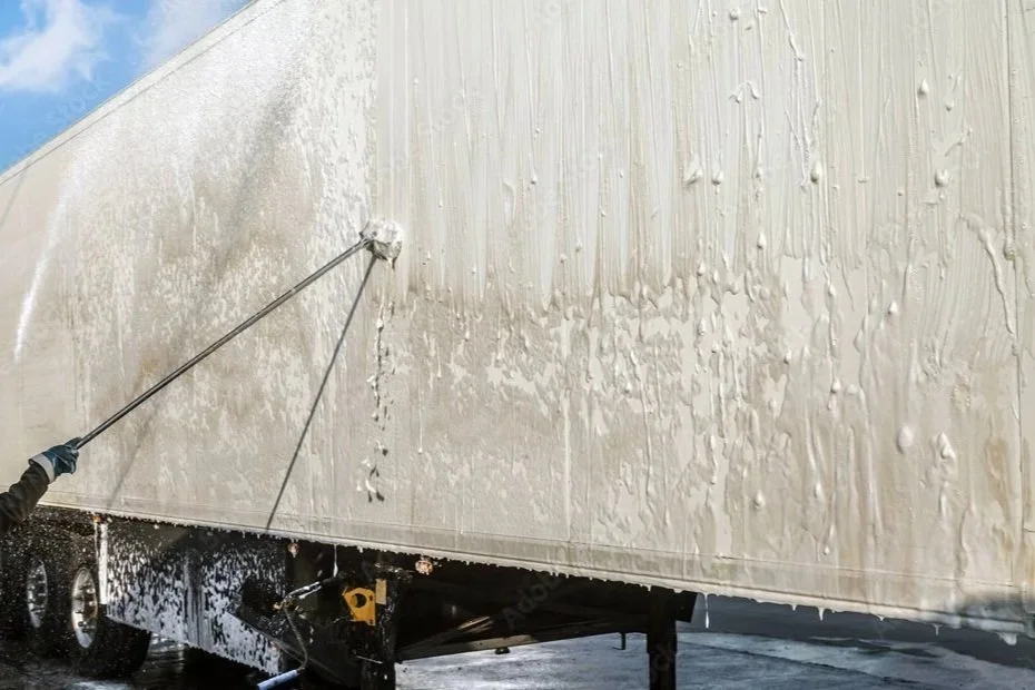 Power washing or cleaning a large white trailer with a high-pressure water spray.