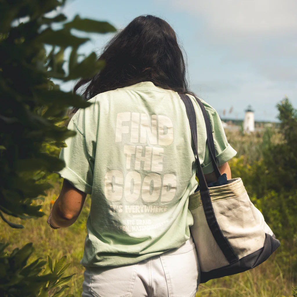 Person wearing light green shirt with the words "Find the Good" walking on a beachside path