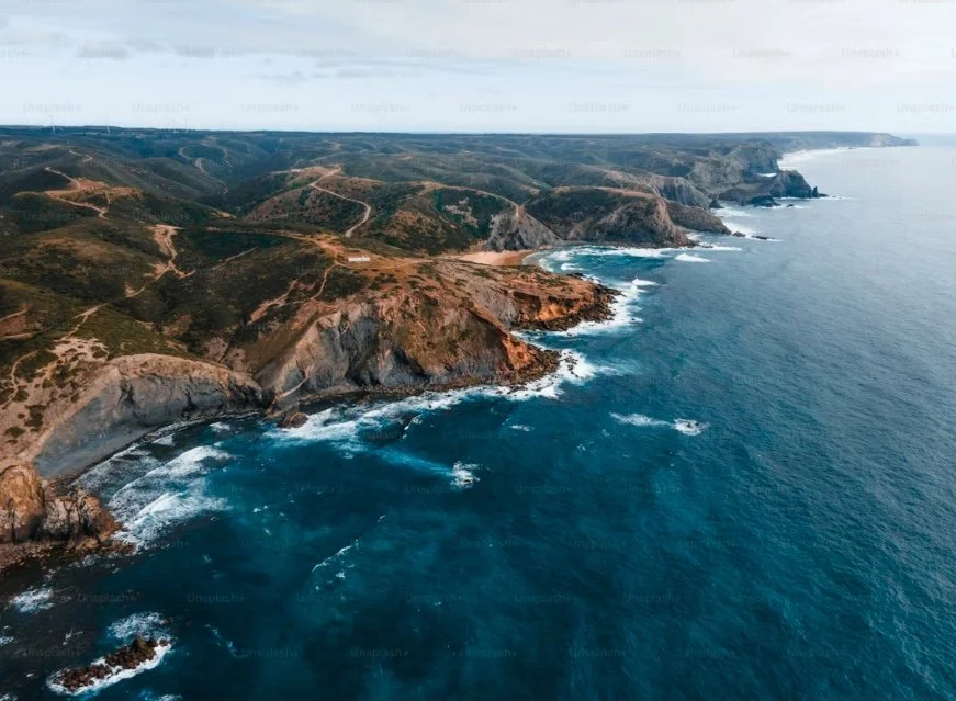 Aerial view of rugged coastline with cliffs, green hills, and ocean waves