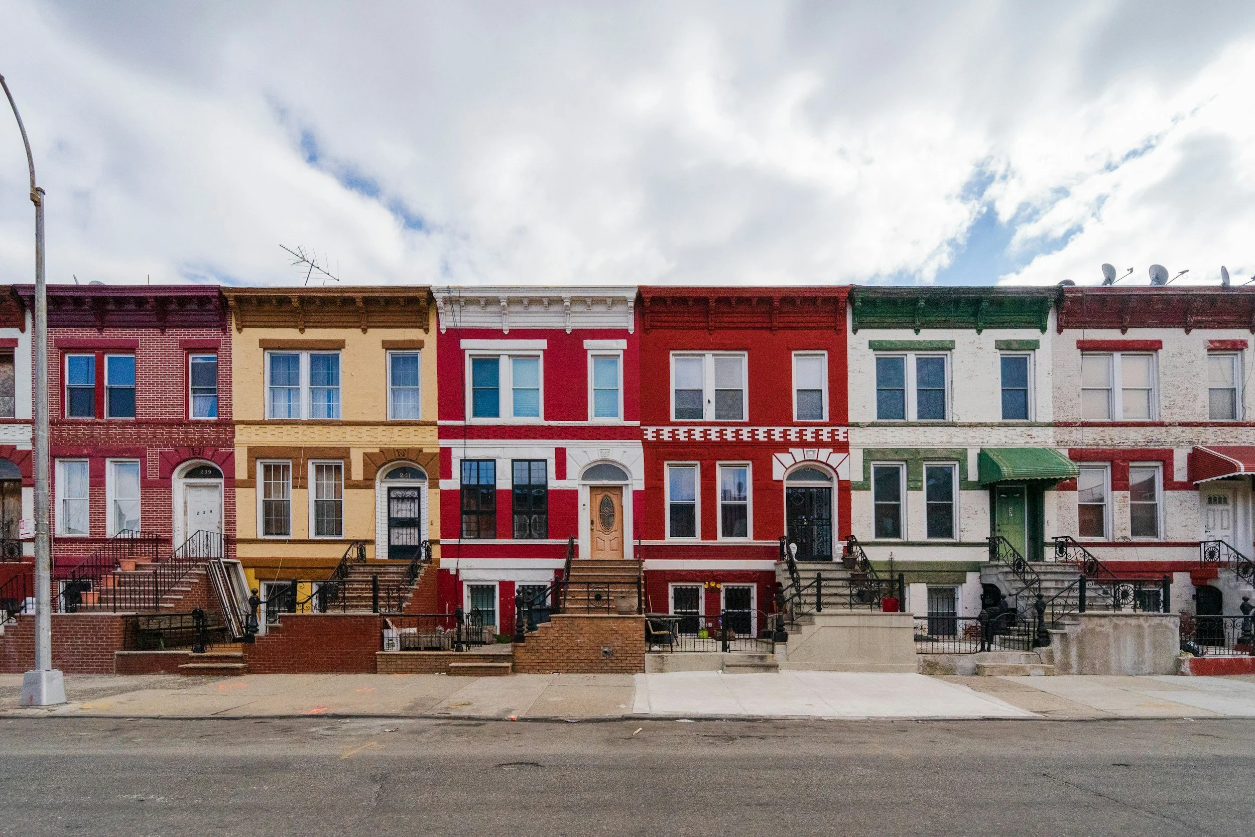A row of colorful historic row houses with decorative facades and front steps along a city street.