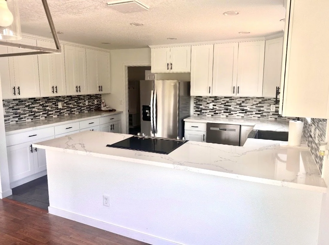 Modern kitchen with white cabinets, a marble countertop, black hardware, a stainless steel refrigerator, a dishwasher, a cooktop, and a granite backsplash.