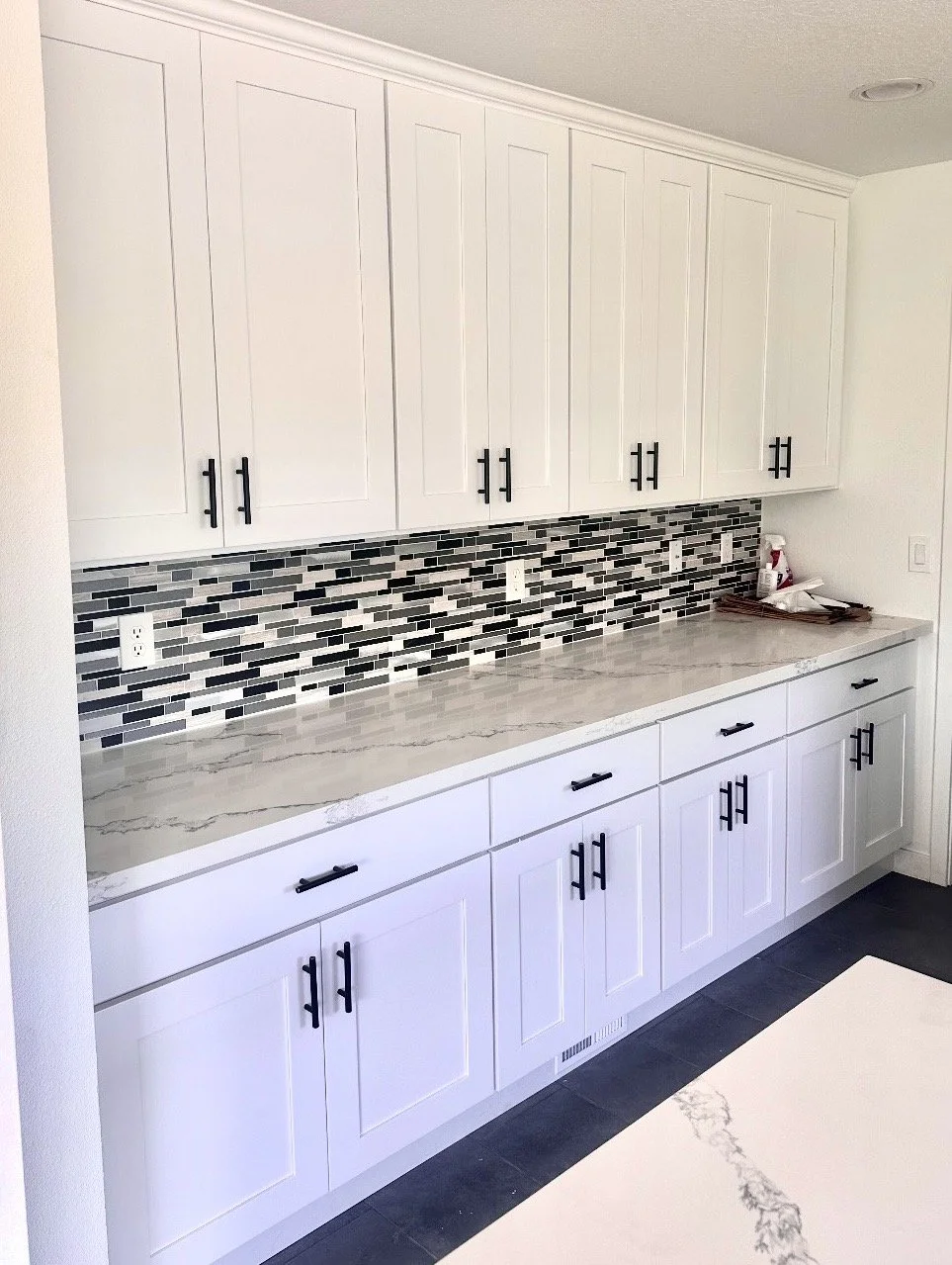 Kitchen counter with white cabinets, black handles, gray marble countertop, and a black and white mosaic tile backsplash.