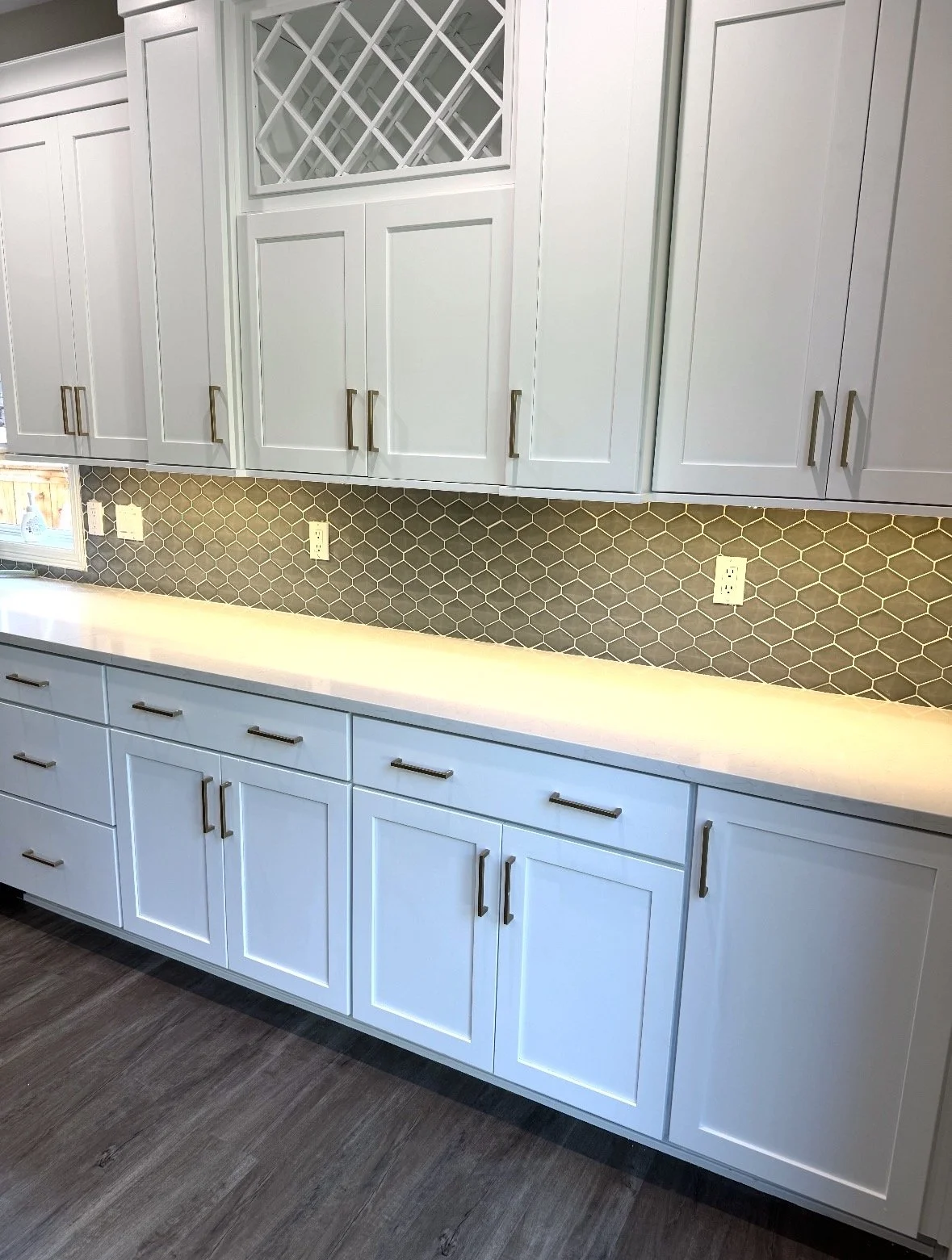 Kitchen cabinet area with white upper and lower cabinets, gold handles, honeycomb tile backsplash, and a light-colored countertop.