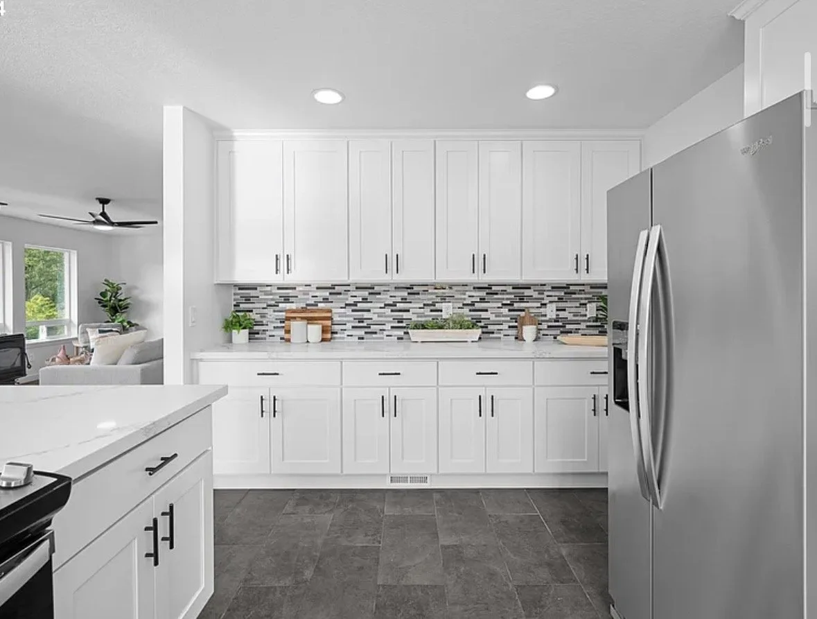 Modern kitchen with white cabinets, colorful mosaic tile backsplash, stainless steel refrigerator, and dark tile flooring.