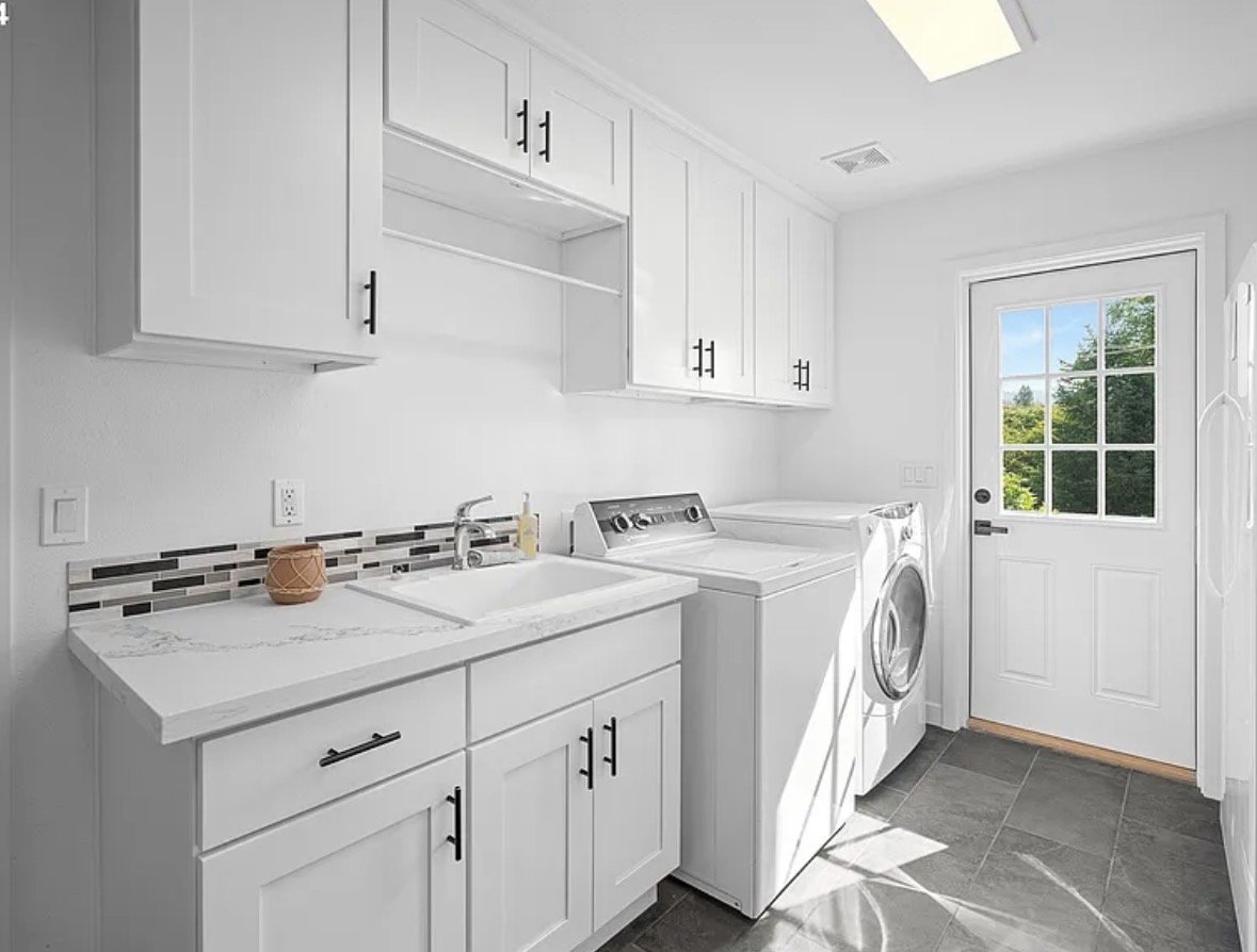 Laundry room with white cabinets, a sink, a washer, a dryer, and a door with a window leading outside, sunlight on floor.