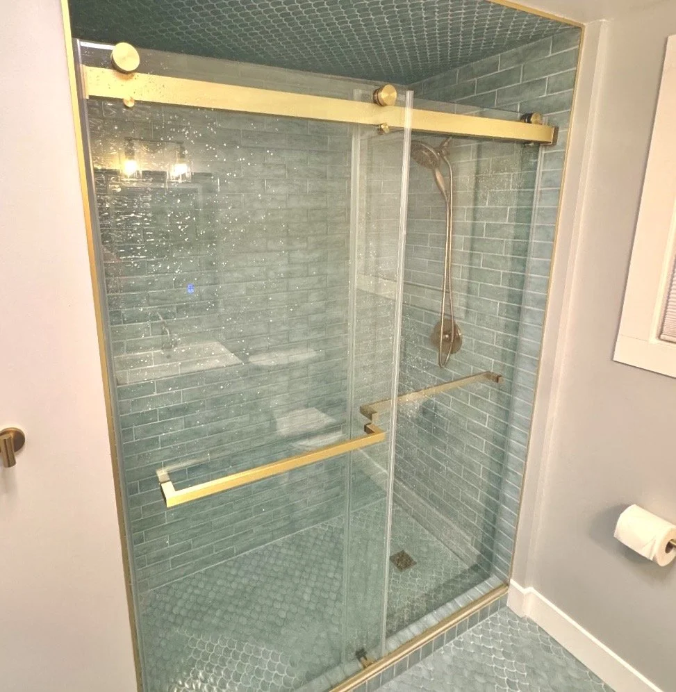 A glass shower enclosure with brass hardware, blue tiled walls, and a handheld showerhead inside.