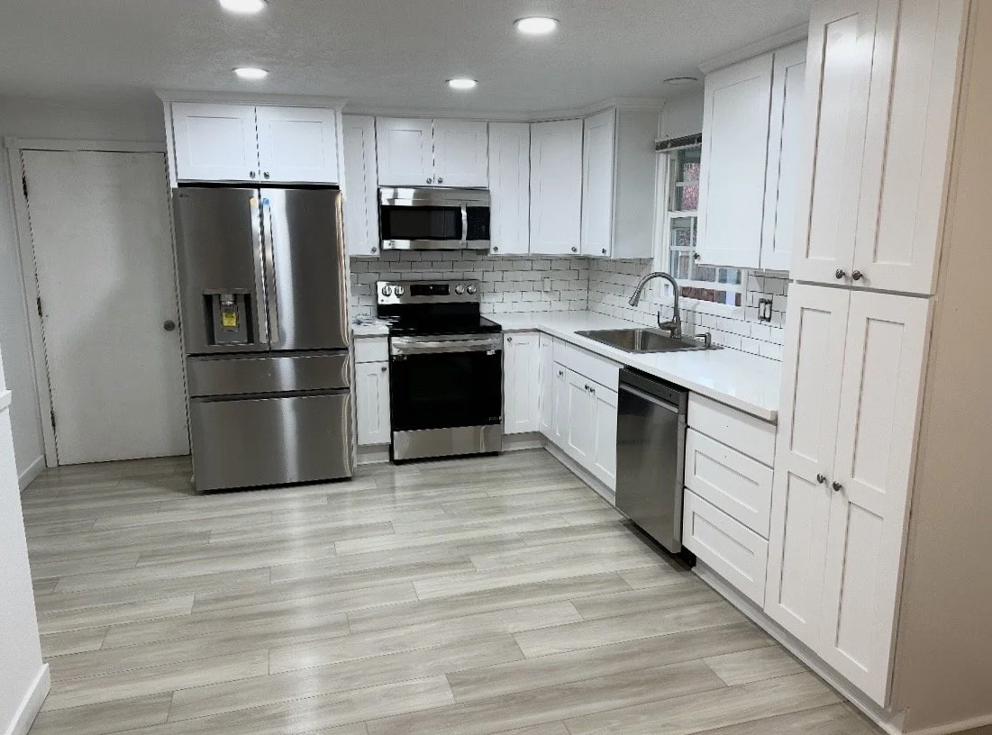 Modern kitchen with white cabinets, stainless steel refrigerator, oven, microwave, dishwasher, and a sink under a window.