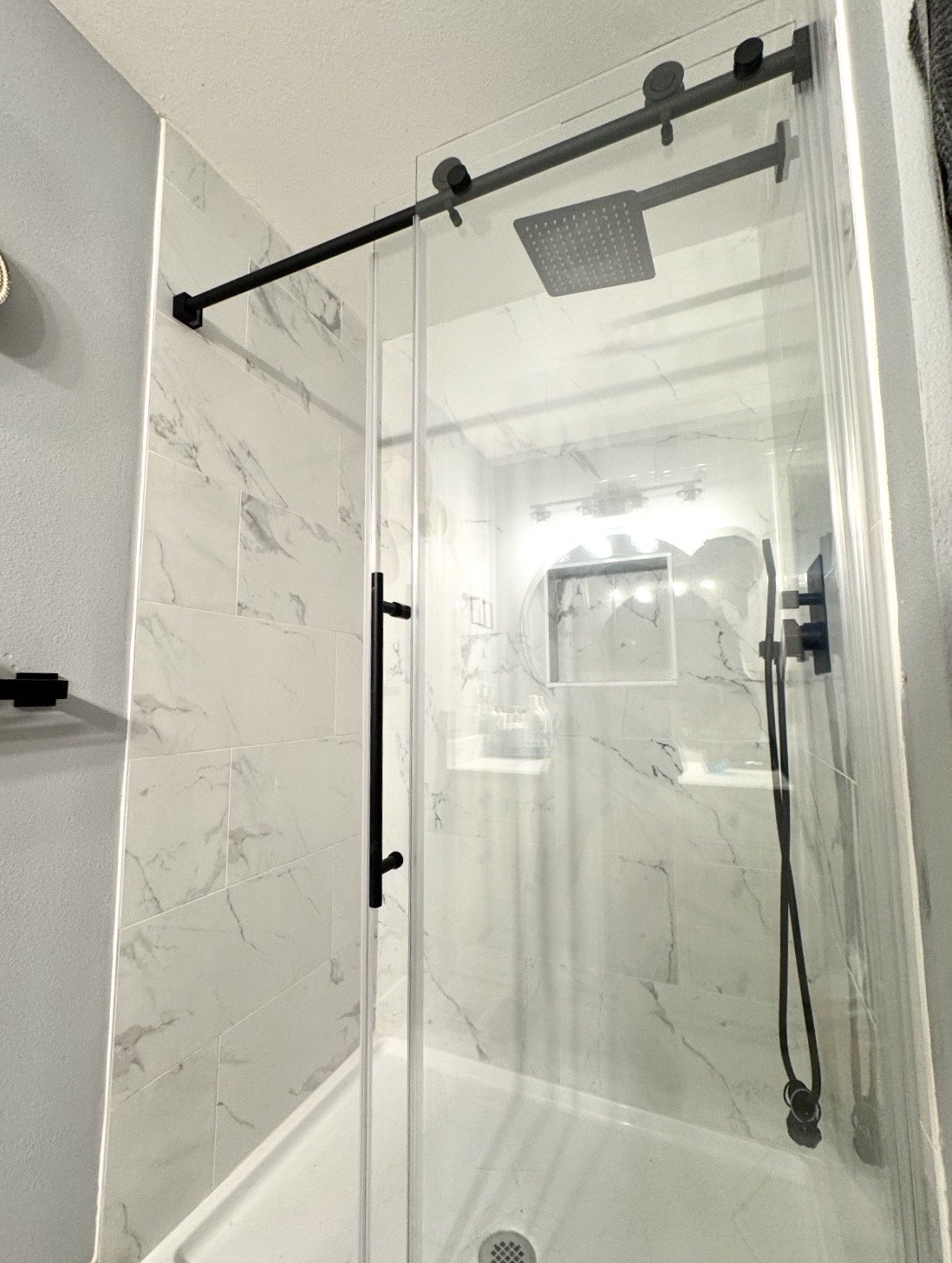 Shower with black hardware, a rainfall showerhead, a handheld shower wand, and marble tiles on the walls.
