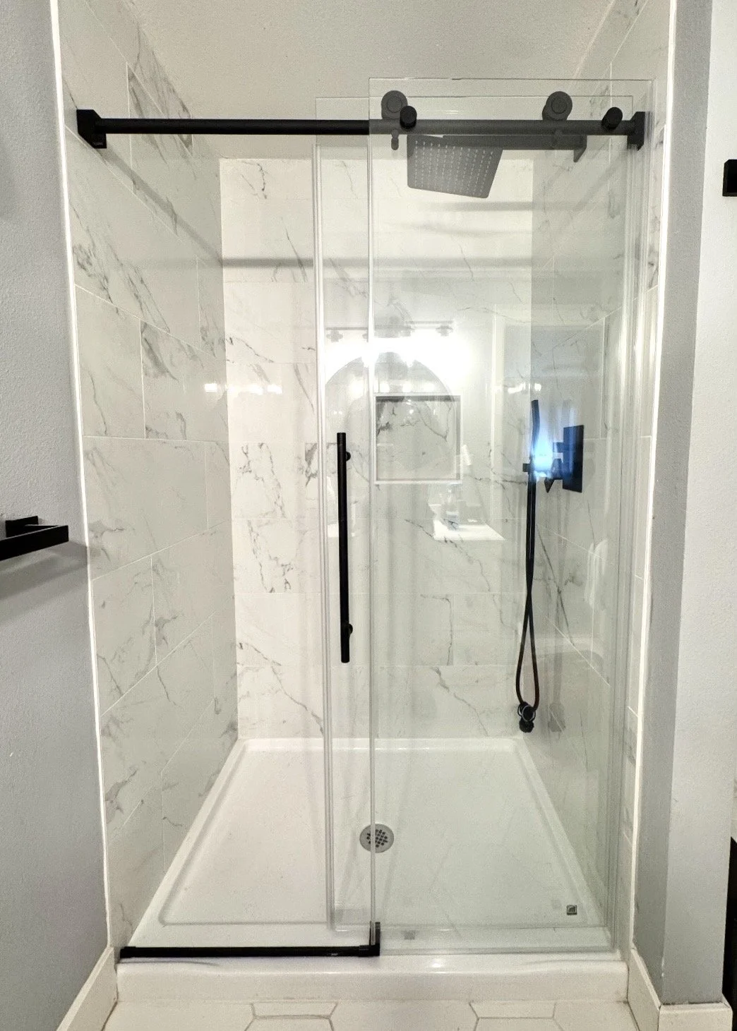 Modern glass shower enclosure with black hardware and marble wall tiles.