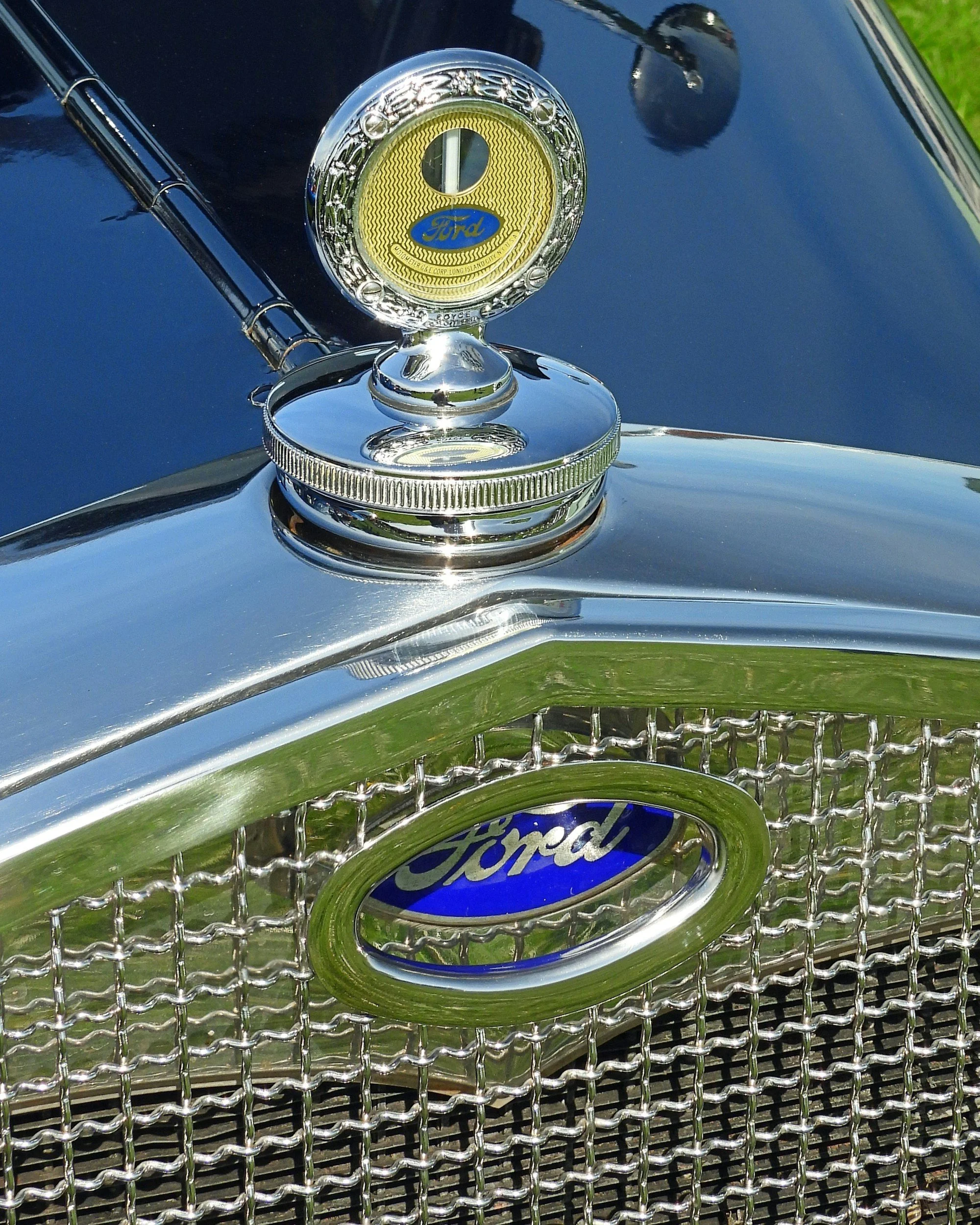 Close-up of a vintage Ford car grille with a chrome hood ornament featuring the Ford logo in the center and a circular emblem on the top of the hood.