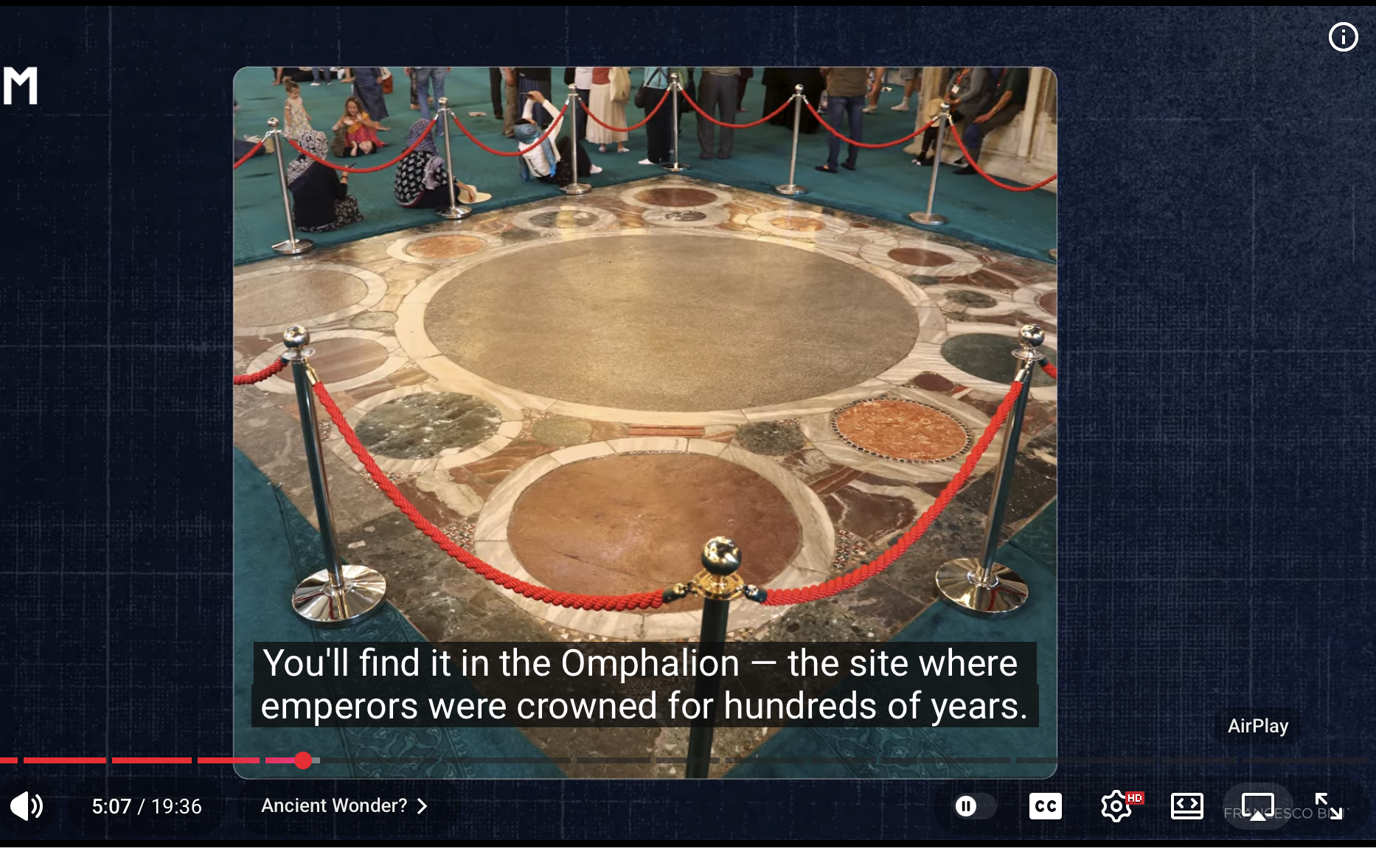 Circular marble floor with decorative inlays, surrounded by a red velvet rope barrier and visitors in a museum.