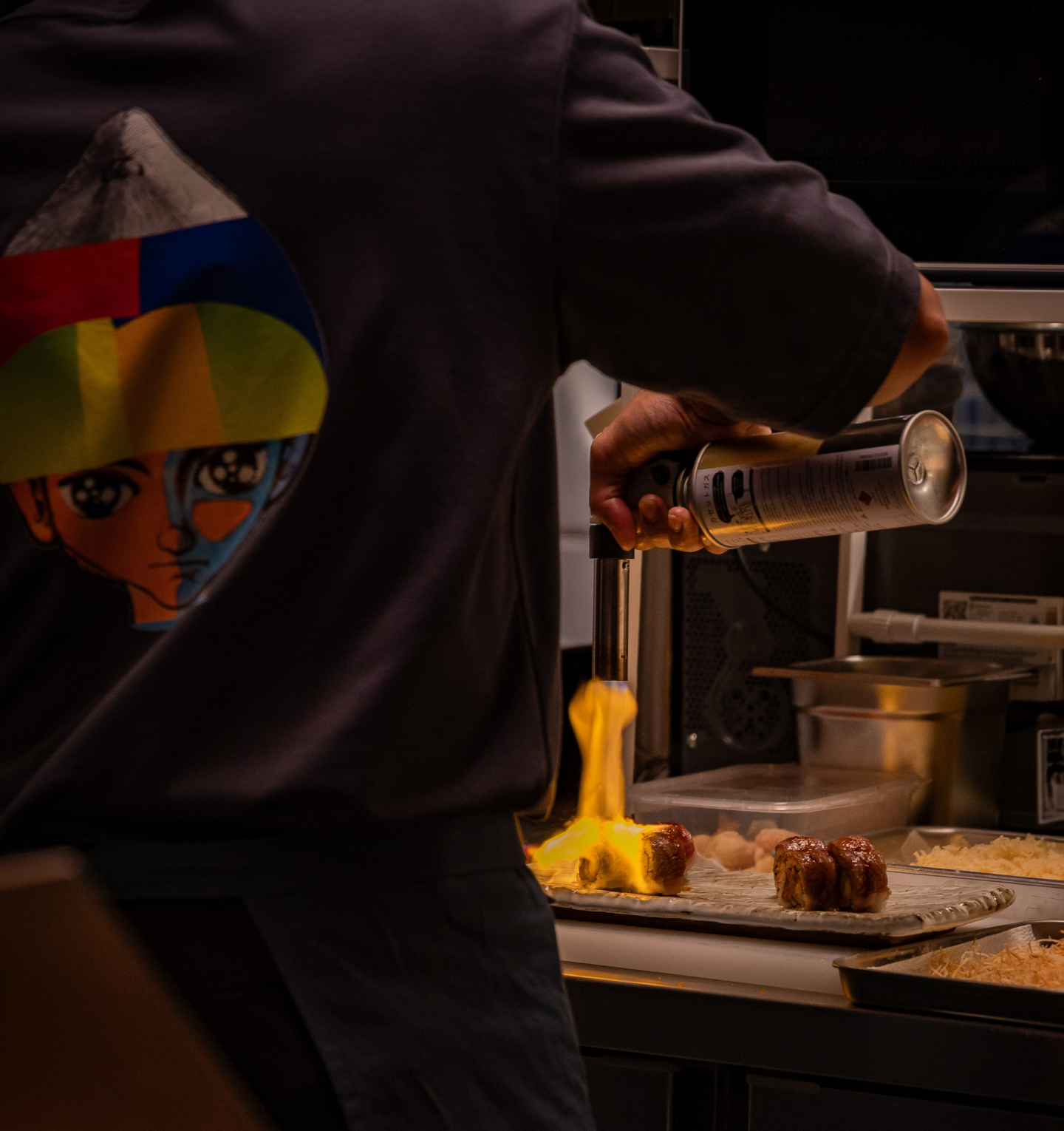 Person pouring a can of spray into a flame, cooking sausages in a kitchen.
