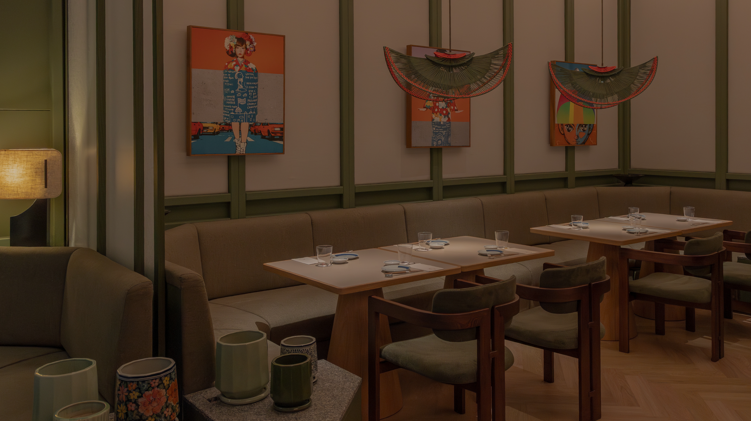 Empty restaurant with art on the wall, tables set with glasses and utensils, warm lighting.