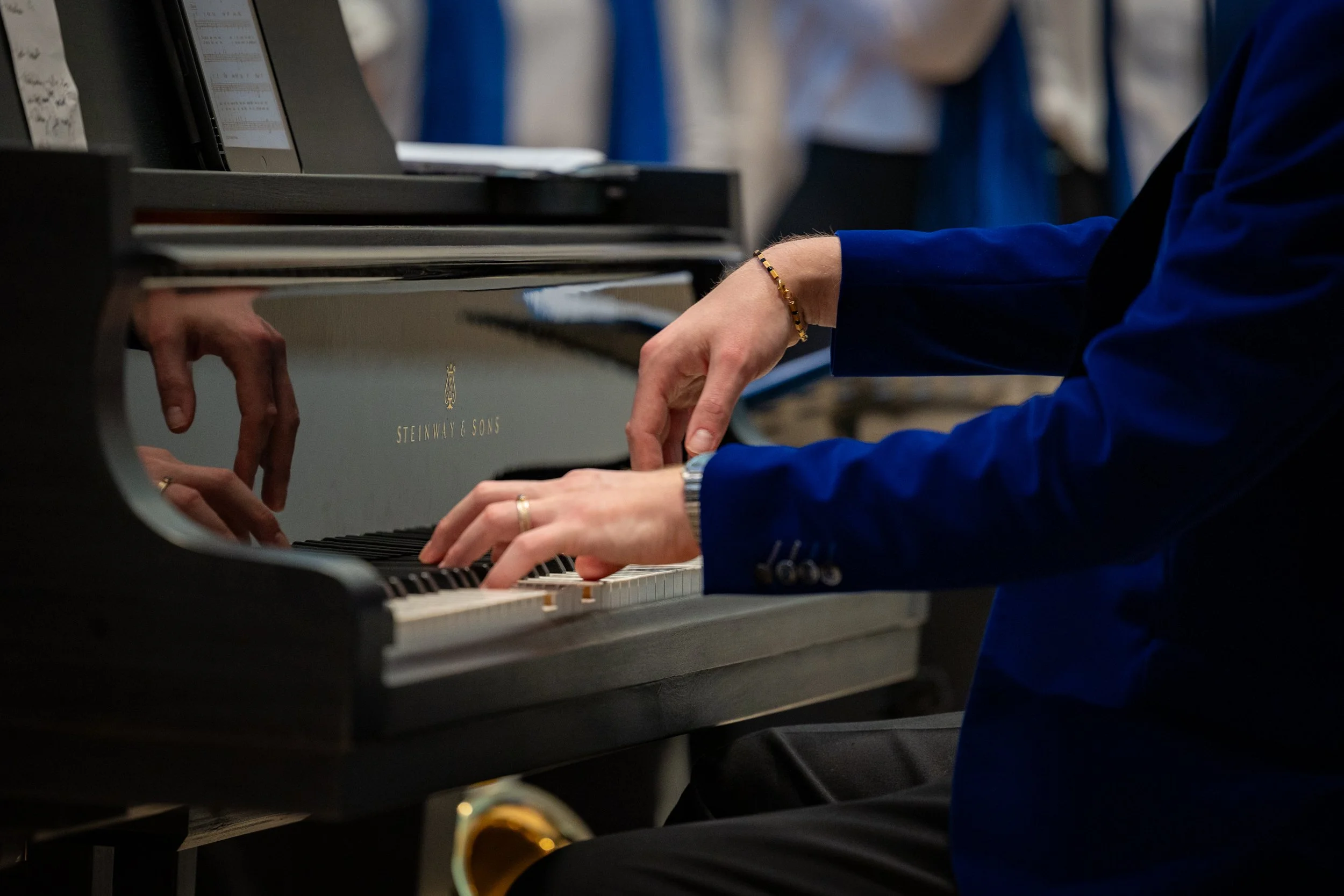 Person in blauer Jacke spielt Klaviers an einem schwarzen Flügel mit Markenlogo 'Steinway & Sons'. Eventfotografie