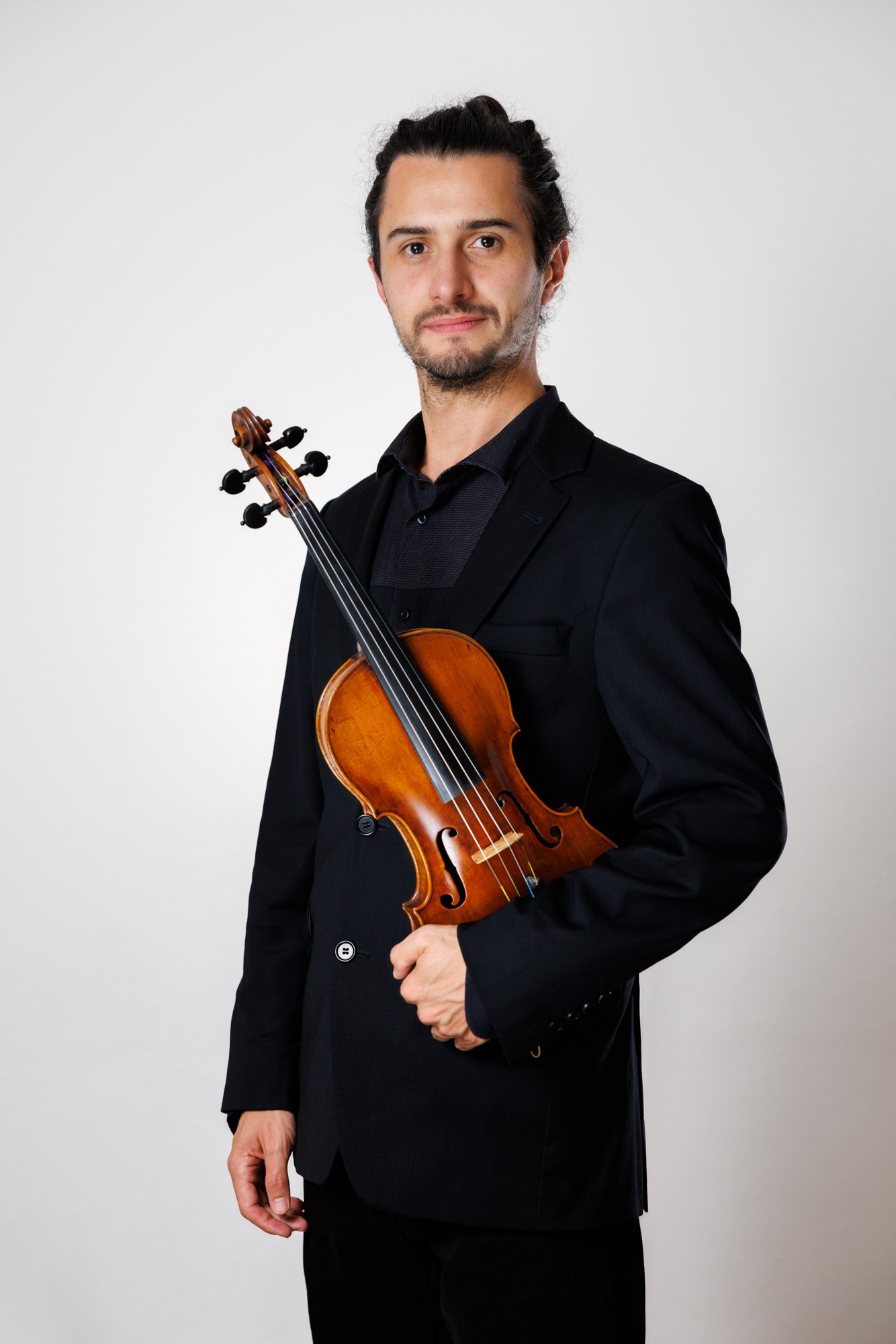 Junger Mann im schwarzen Anzug, hält eine Geige, vor hellem Hintergrund. Porträt