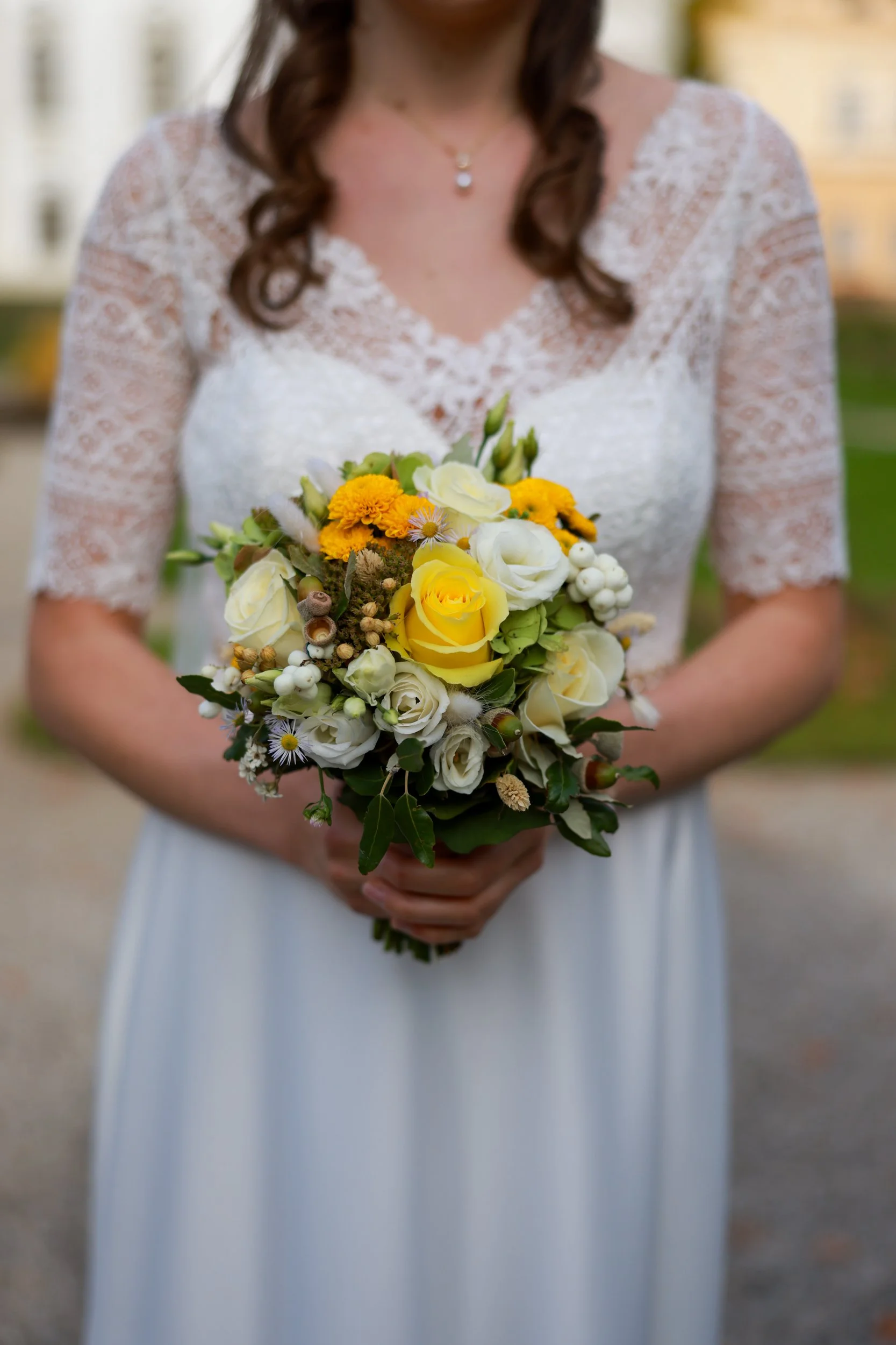 Braut hält einen Blumenstrauß aus gelben und weißen Blumen und Grün.
