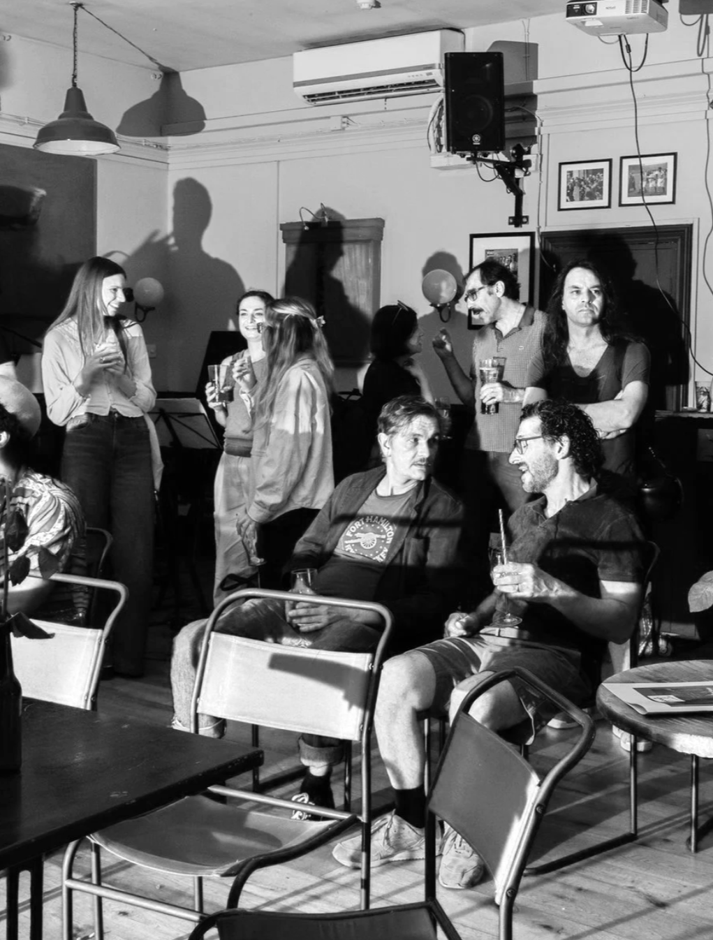 Group of people socializing and enjoying drinks in a bar or restaurant with framed pictures on the wall.