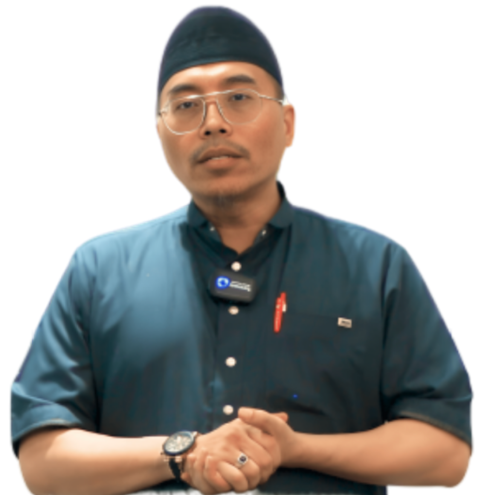 A man wearing glasses, a black cap, a dark blue collared shirt with a badge, watch, and pen, standing with hands clasped in front of him against a black background.