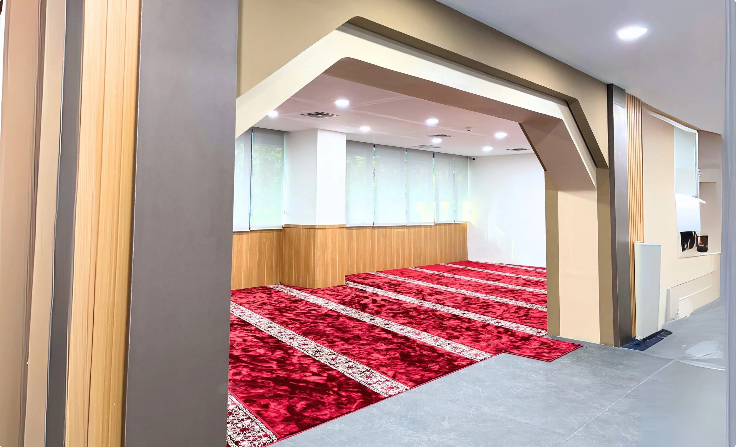 Empty prayer room or mosque with red carpet and large windows.