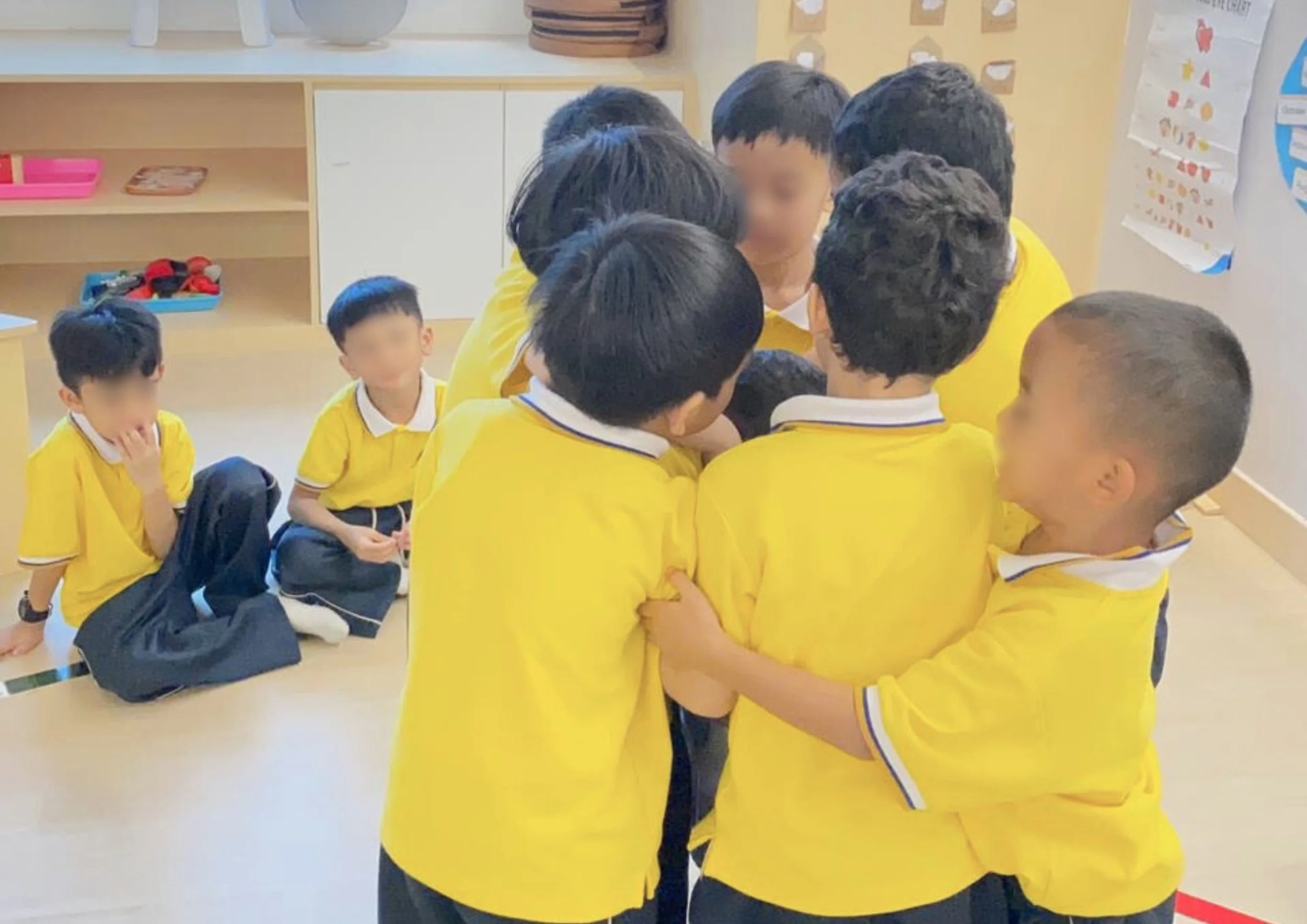 A group of children in yellow uniforms gathered together, playing or interacting closely in a classroom.