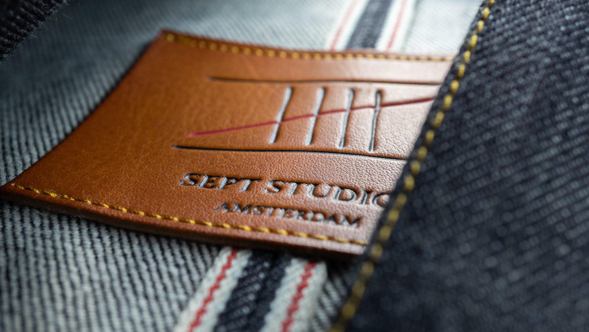 Close-up of a leather patch sewn onto denim fabric, with the text 'SEPT STUDIOS' and 'AMSTERDAM' visible.