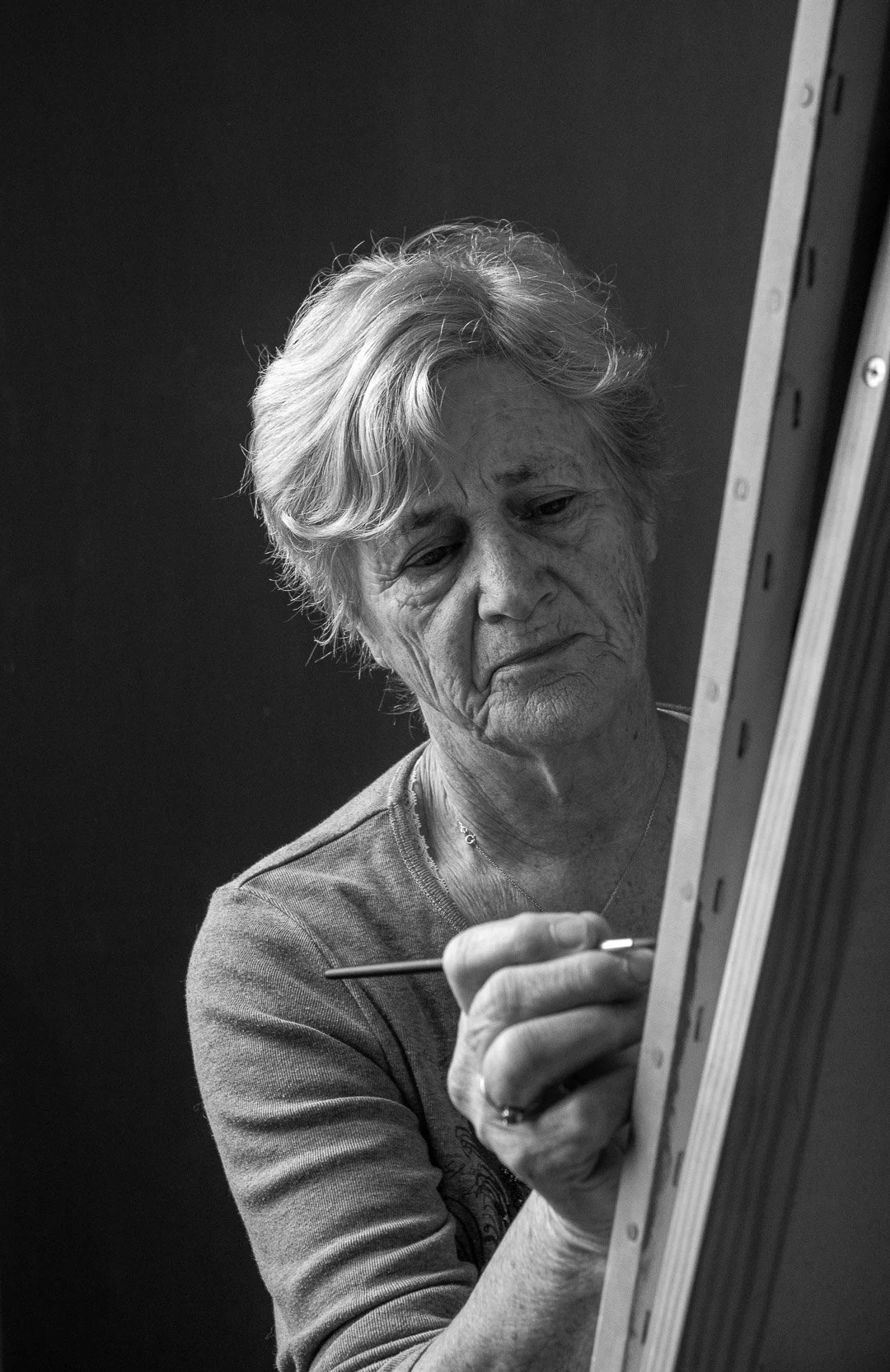 Une femme âgée peint sur une toile, concentrée, en noir et blanc.