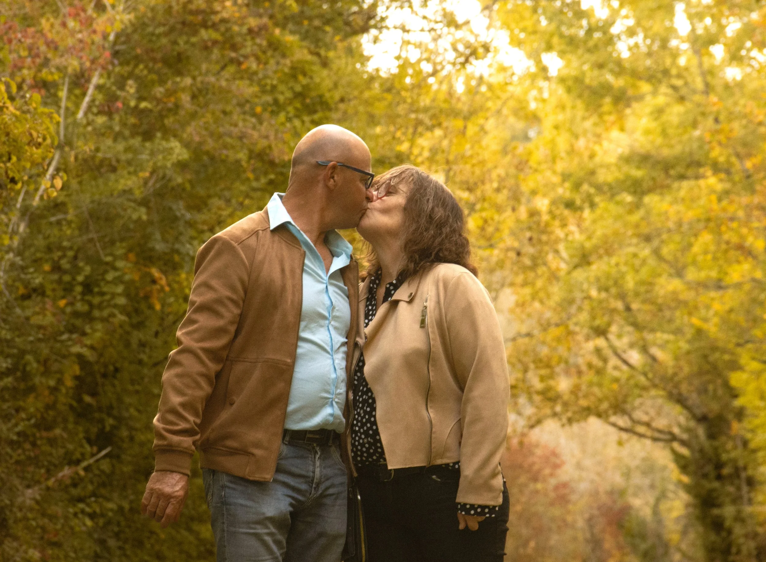 Un couple s'embrassant dans un parc aux arbres aux feuilles d'automne en arrière-plan.